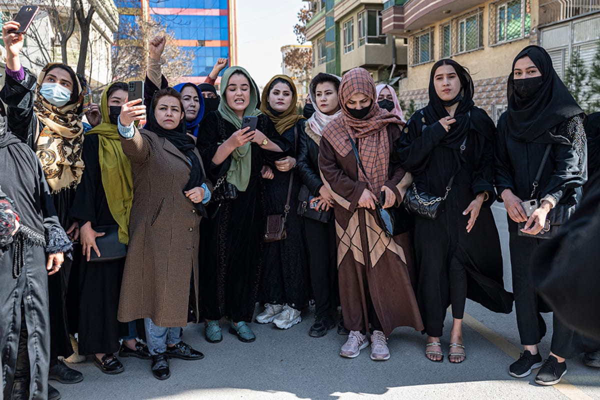 Women standing in an urban area wearing headscarves while speaking and holding mobile phones.