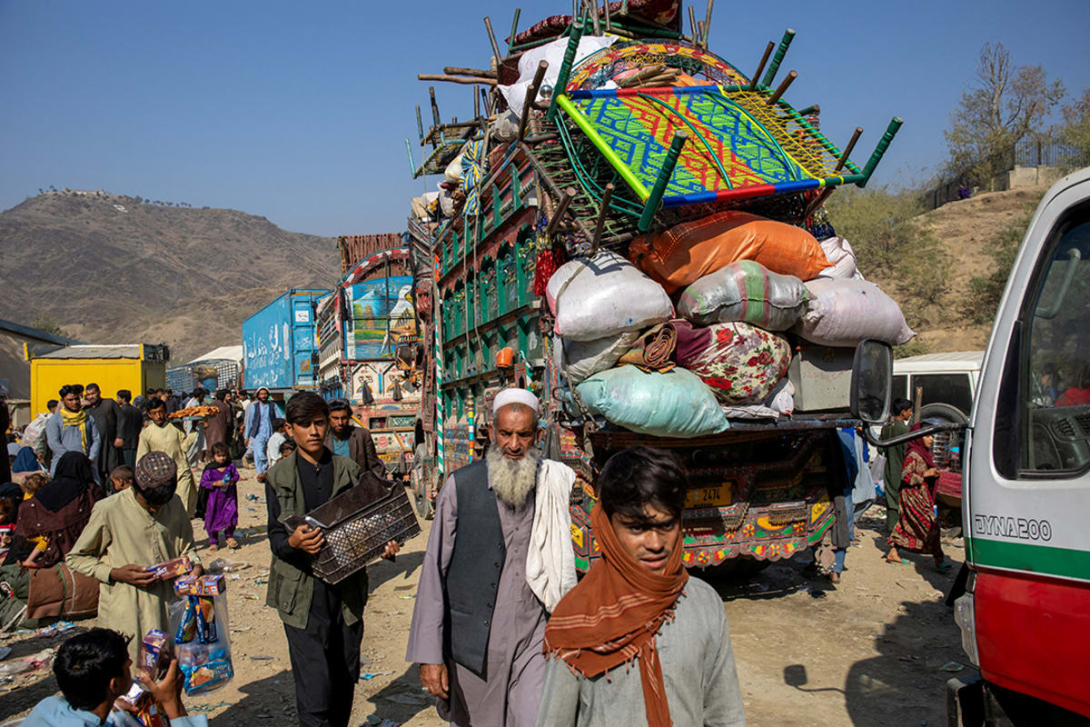 People walk along a caravan of vehicles packed with belongings.