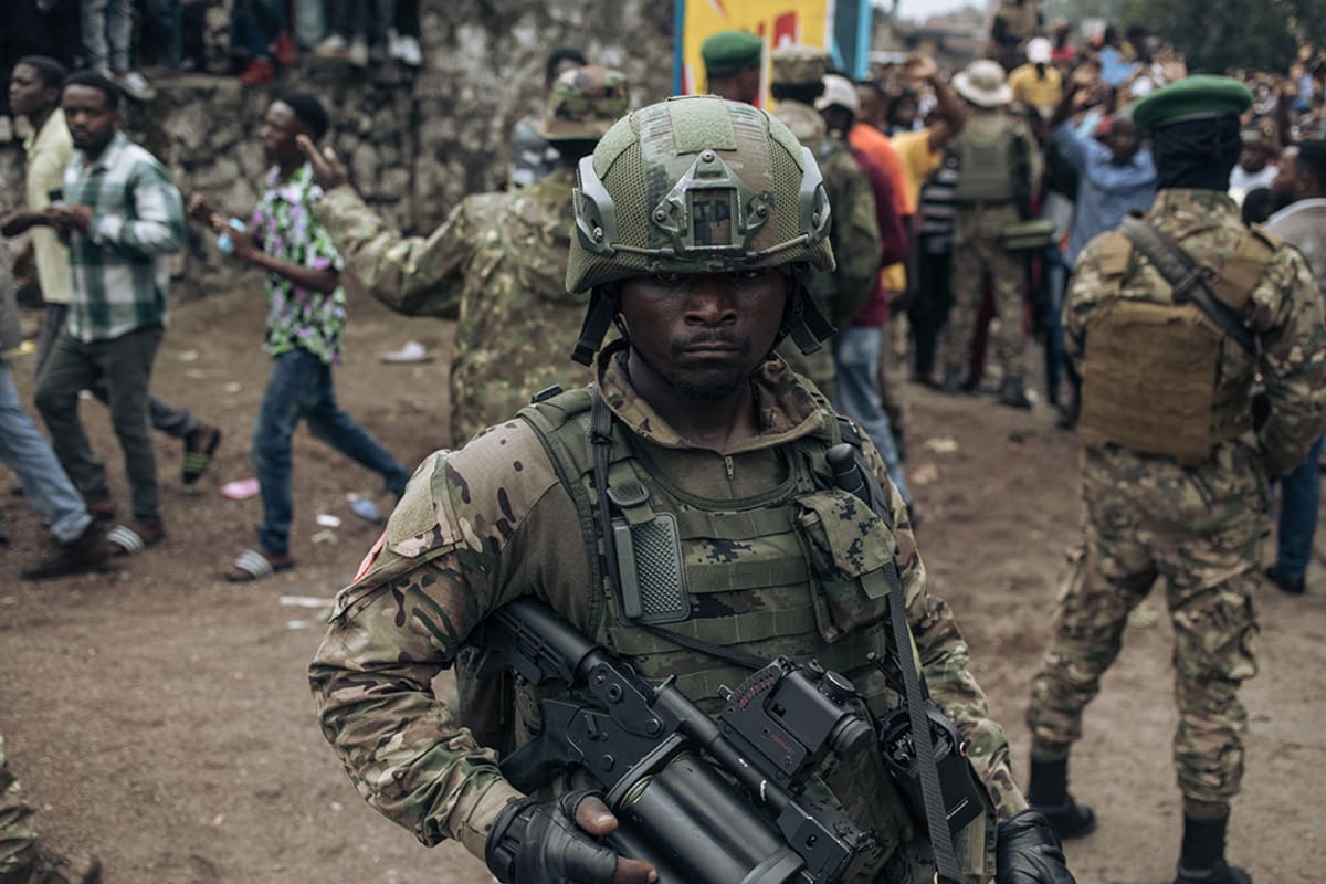A soldier wearing green fatigues and carrying a gun watches over a crows