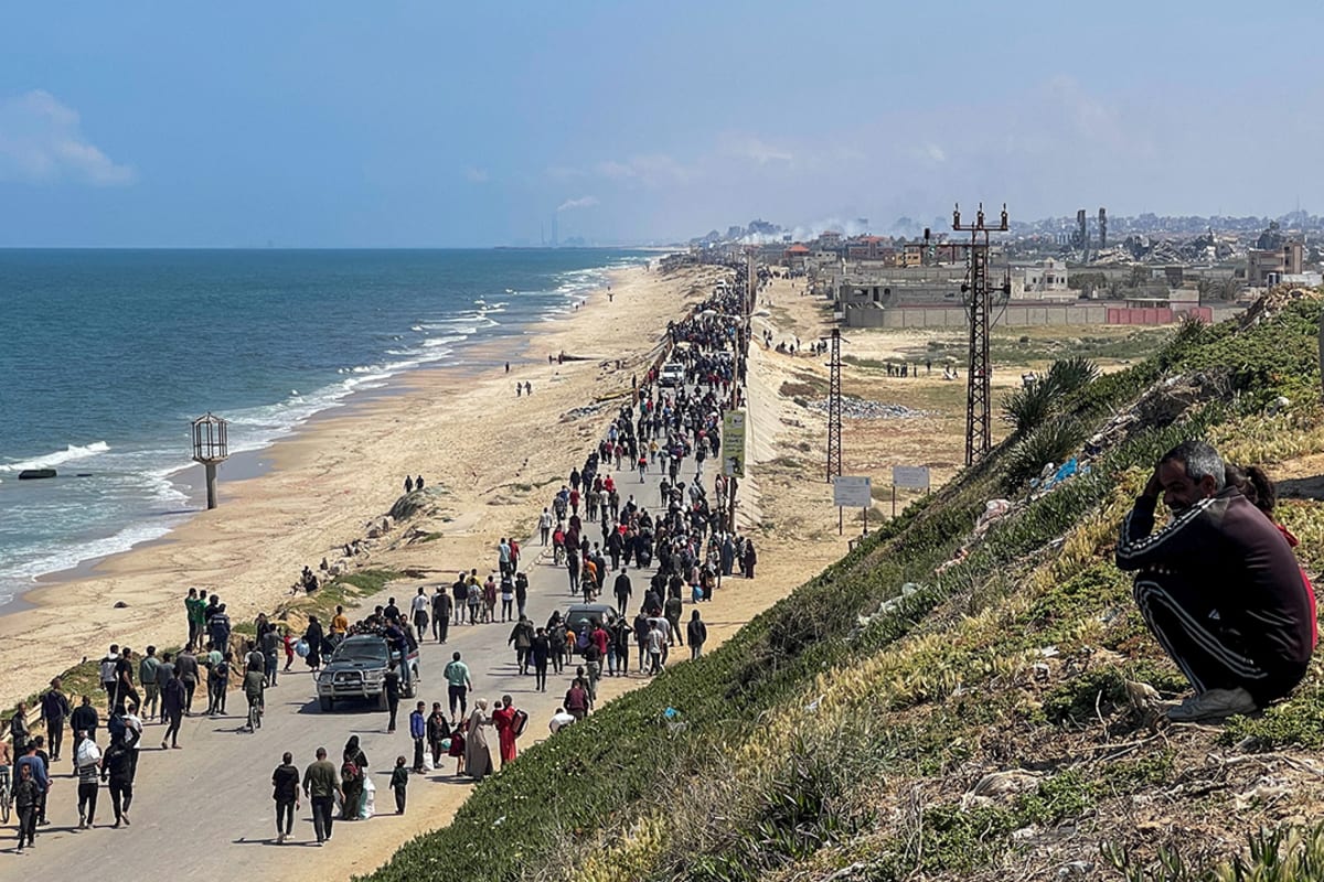 People walk alongside a coastline carrying belongings.