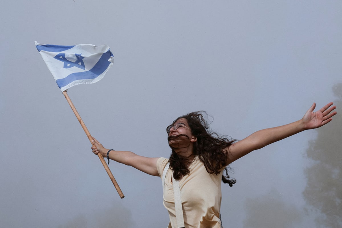 A woman stands with her arms outstretched holding an Israeli flag.