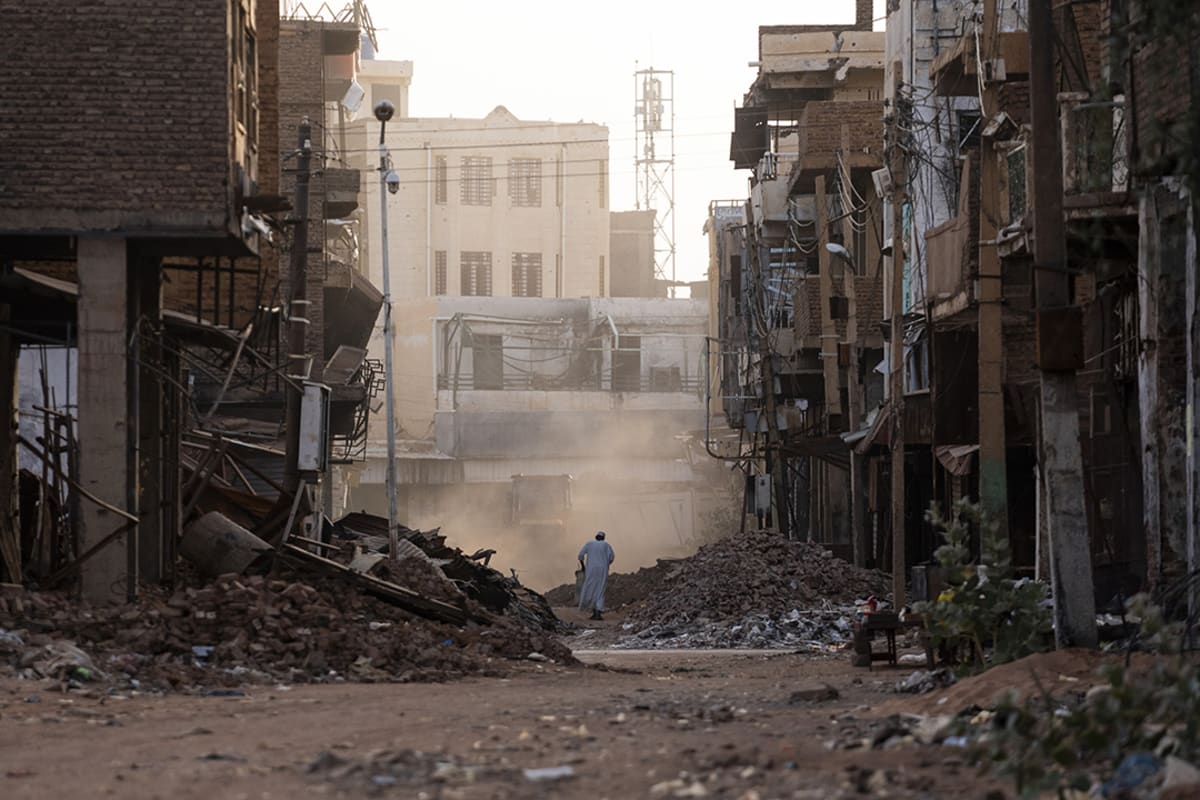 A person walks amid the rubble of buildings in an urban area.