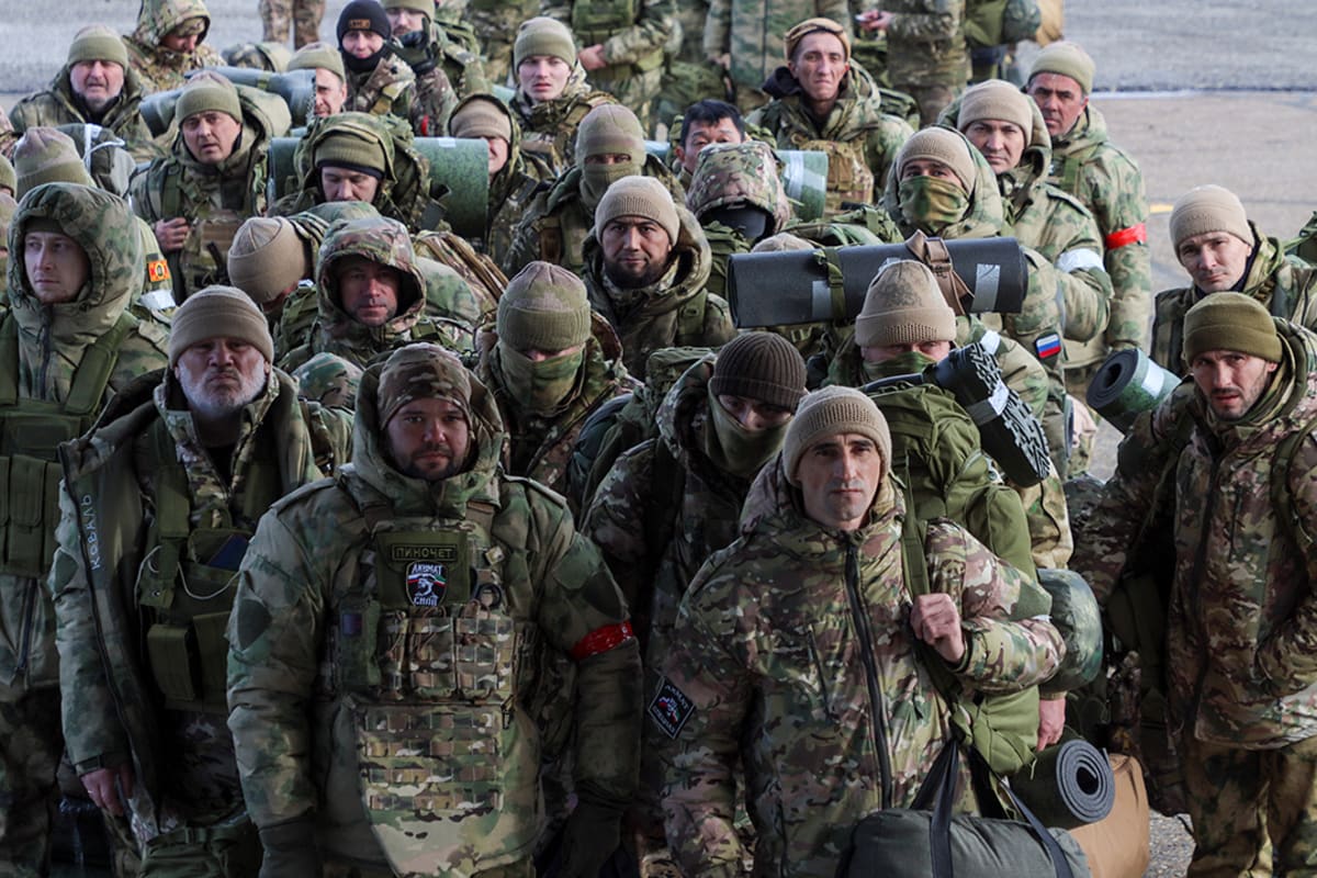 Soldiers stand together in a huddle while carrying belongings.