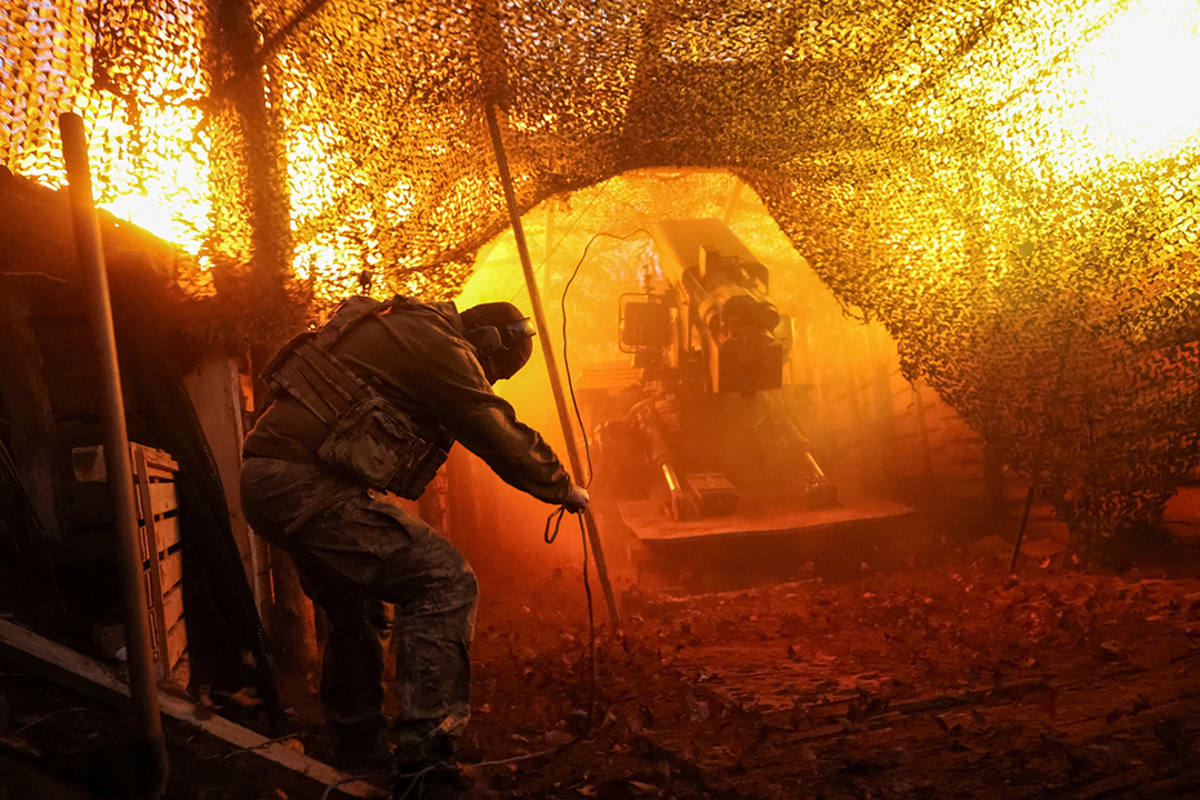 A soldier faces away from the camera while launching a howitzer.