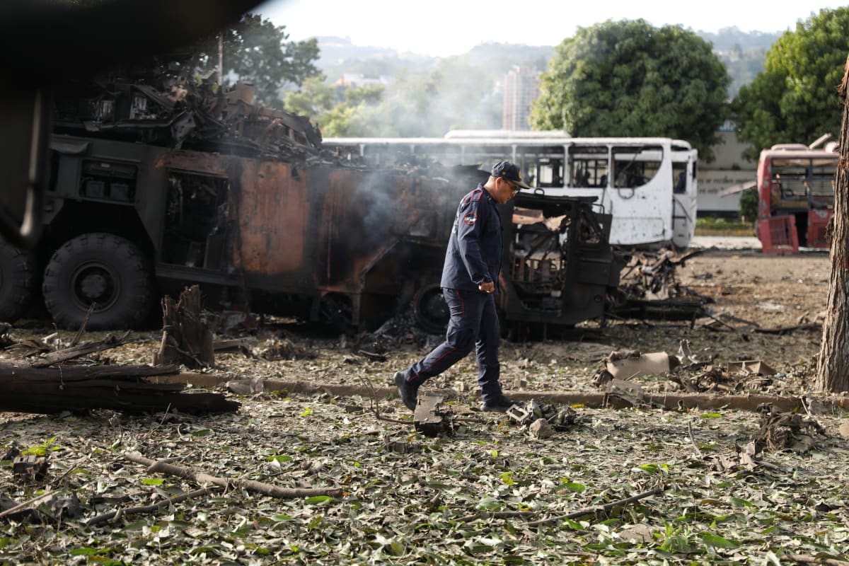 A man walks past a burned out tank.