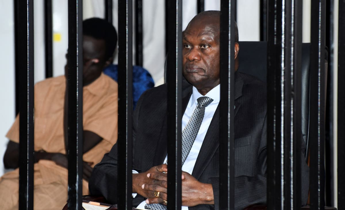 A man wearing a suit sits inside a black steel cage.