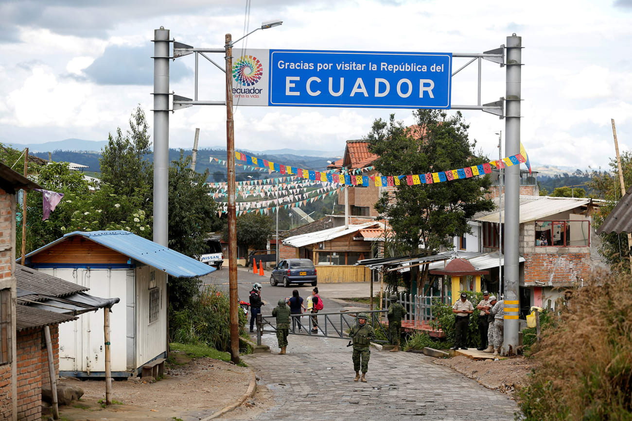 Soldiers guard the Ecuadoran side of a border with Colombia in Tufino, Ecuador on March 15, 2020, after country leaders announced the closure of its borders to all foreign travelers due to COVID-19. The photo shows a simple border crossing through a small town with a big sign reading "Ecuador" above the street. The crossing is closed with metal barricades, and a soldier stands out front. REUTERS/Daniel Tapia