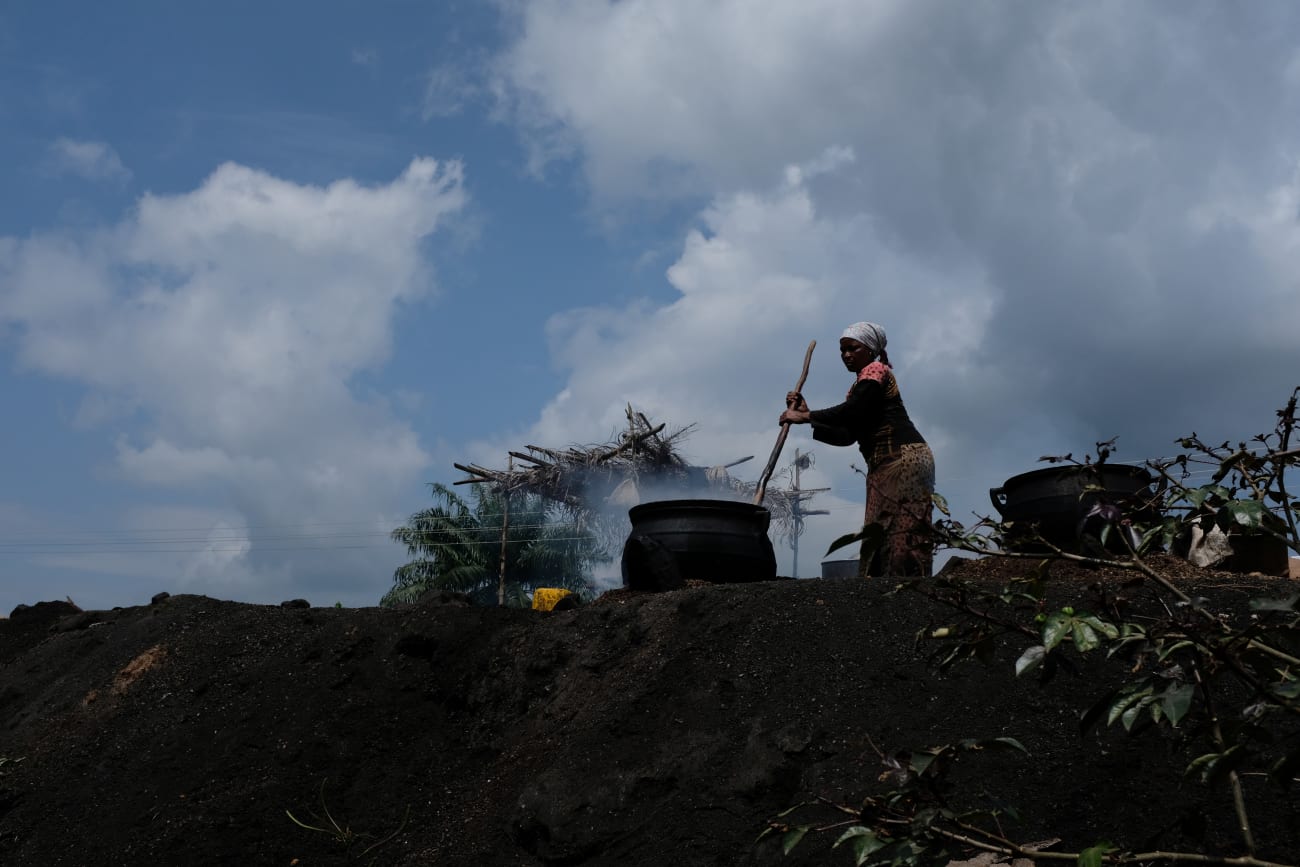 A woman cooks palm nuts to make oil on the road that connects Obuasi to Cape Coast, in Ghana, on July 26, 2019.