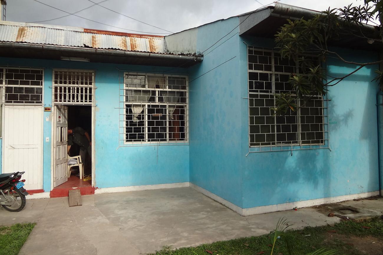 Picture shows a single-story, tin-roof home in town of Iquitos, Peru. The walls are blue, the skies are gray and there's a lonely motorcycle parked in the yard.