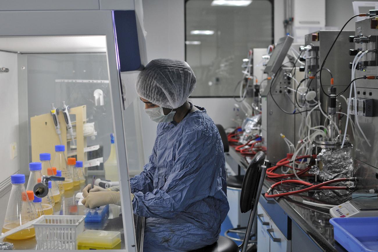 Photo shows a worker in full protective gear working under a ventilation hood.