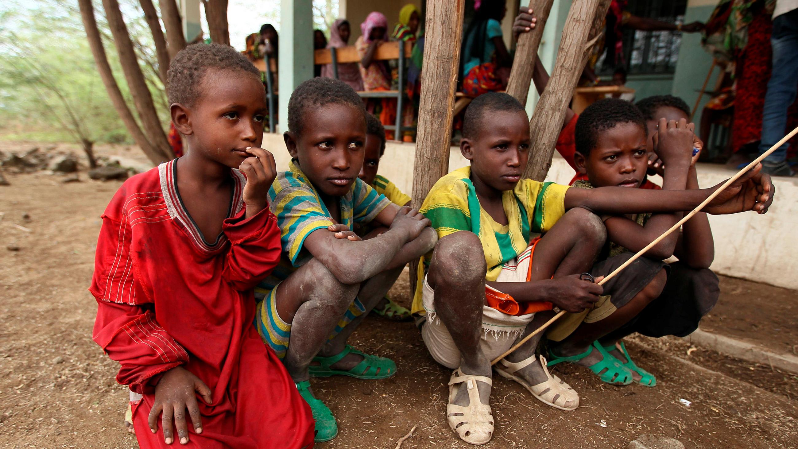 The image shows six pre-teen boys squatting in front of the steps of the center.