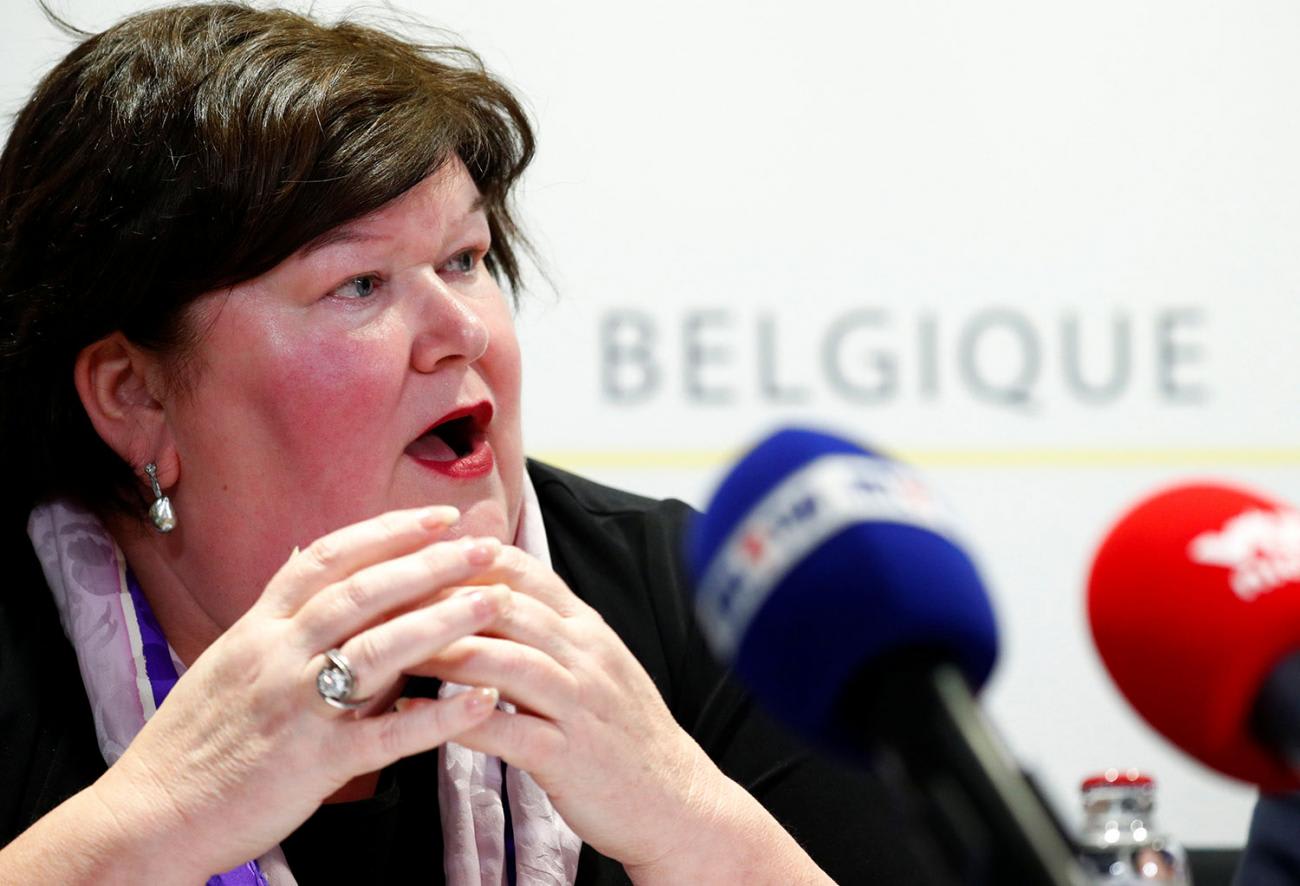 The photo shows the health minister at a table speaking into a microphone.