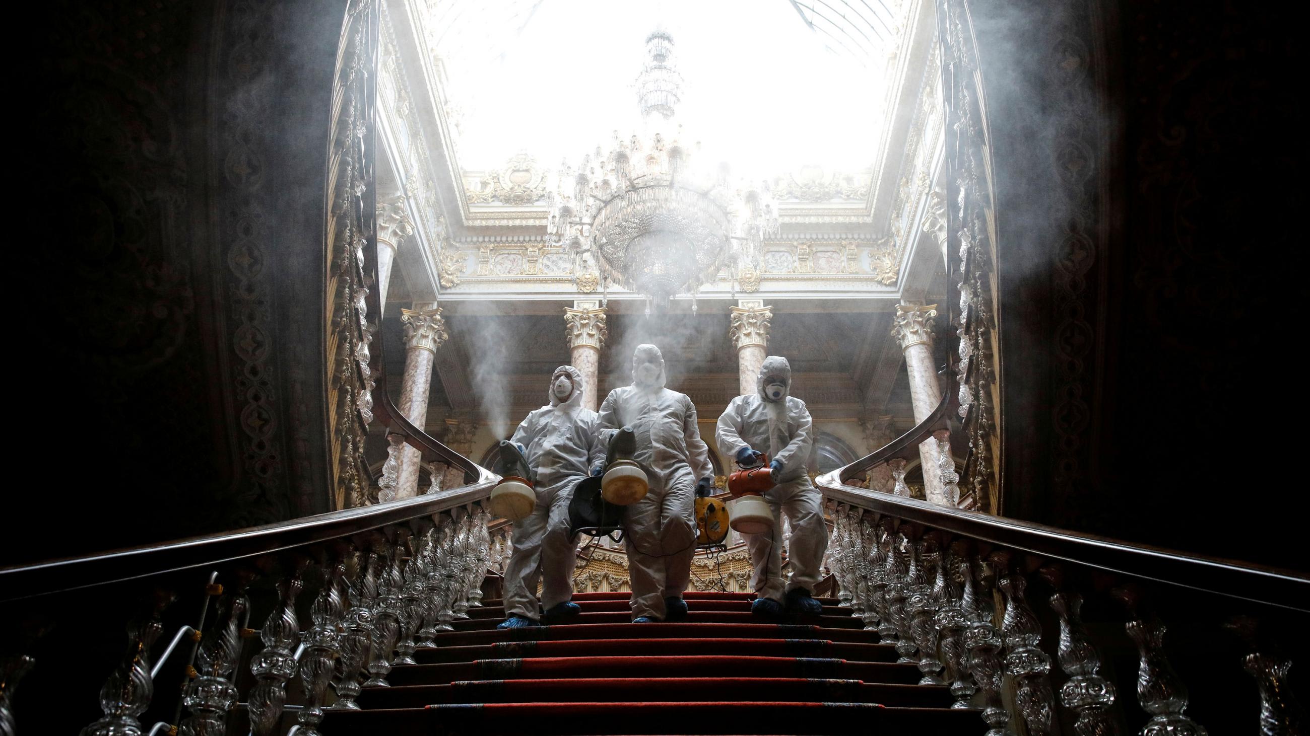 This is a stunning picture of three workers coming down a stunningly beautiful staircase while spraying disinfectant.