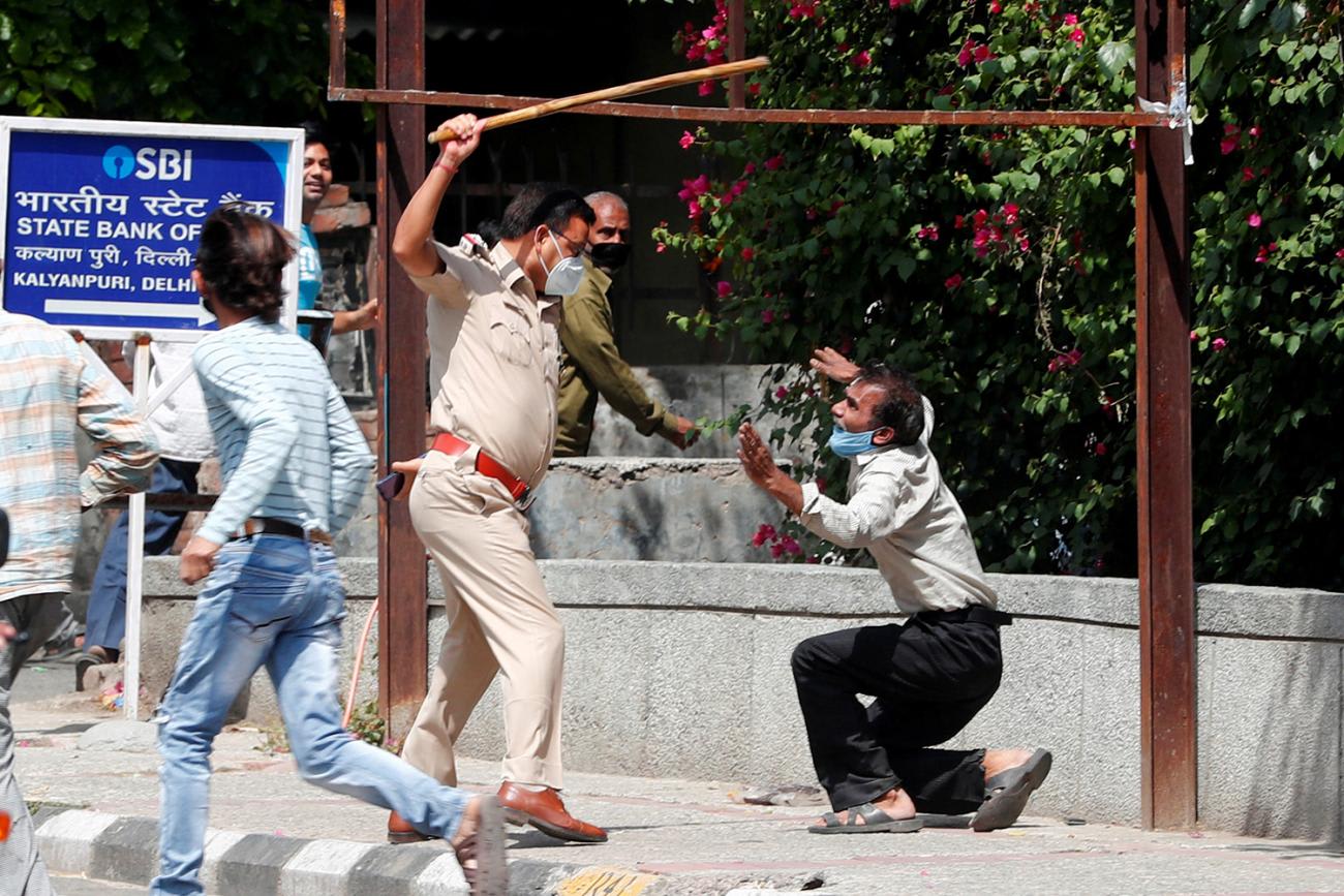 The photo shows a man on his knees appearing to plead with a uniformed officer who has a long baton raised high above his head ready to strike.