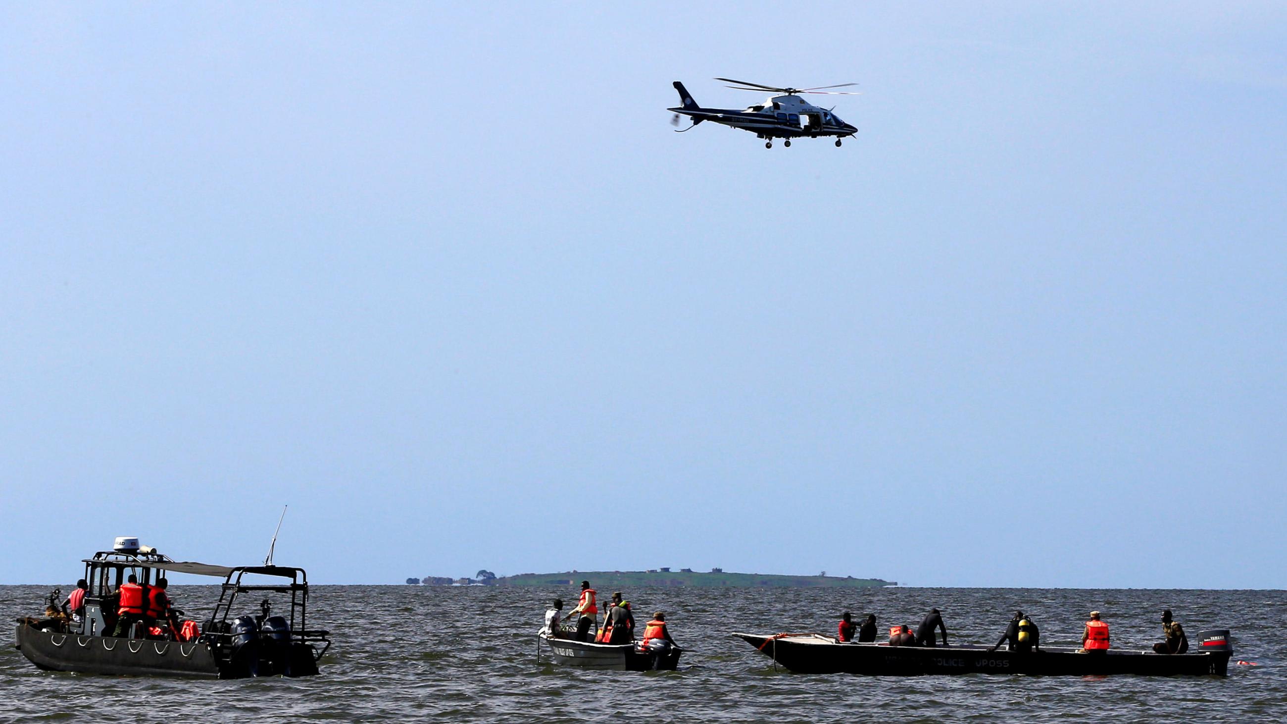 Rescue and recovery missions search for the bodies of dead passengers after a cruise boat capsized in Lake Victoria off Mukono district, Uganda November 25, 2018. Picture shows three motor boats in the water with people standing on their decks. One has a diver partially submerged hanging on to the side. A helicopter flies overhead.