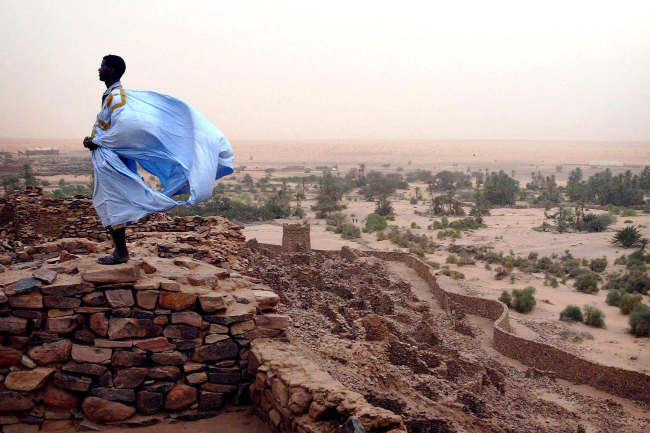 A Mauritanian man stands on what appears to be an ancient wall of old baked bricks on Aug 16, 2005 in the ancient village of Ouadane. He is wearing a light blue robe that is filling with strong winds, presumably carrying sand and dust south from the Sahara, and stands in bright contrast to the dull red background. Africa's Sahel region is threatened by desertification. REUTERS/Finbarr O'Reilly