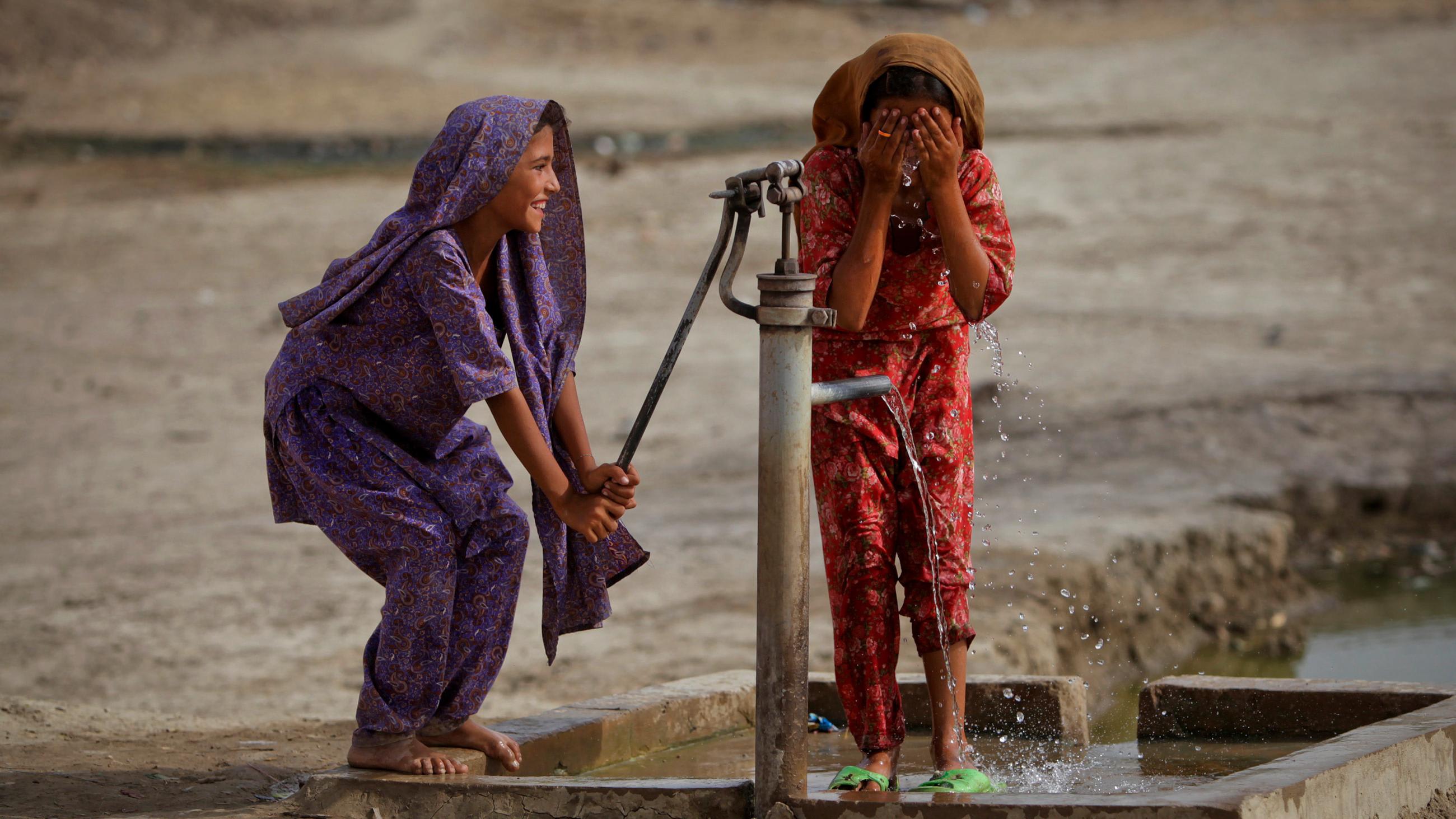 The picture shows two girls, one pumping, the other washing, and both laughing.