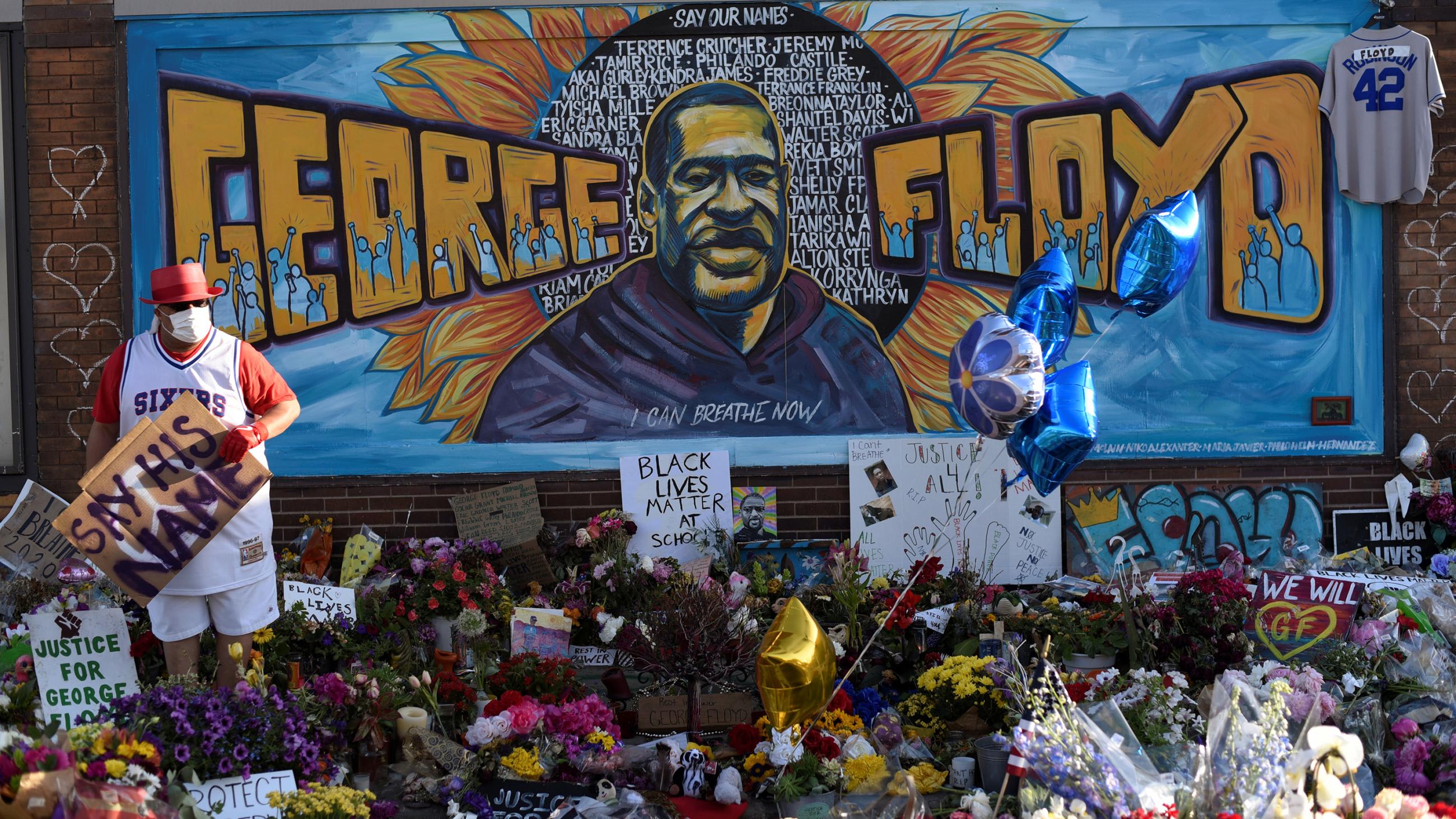 The photo shows a mural to Floyd with lots of flowers and signs laid out in front.