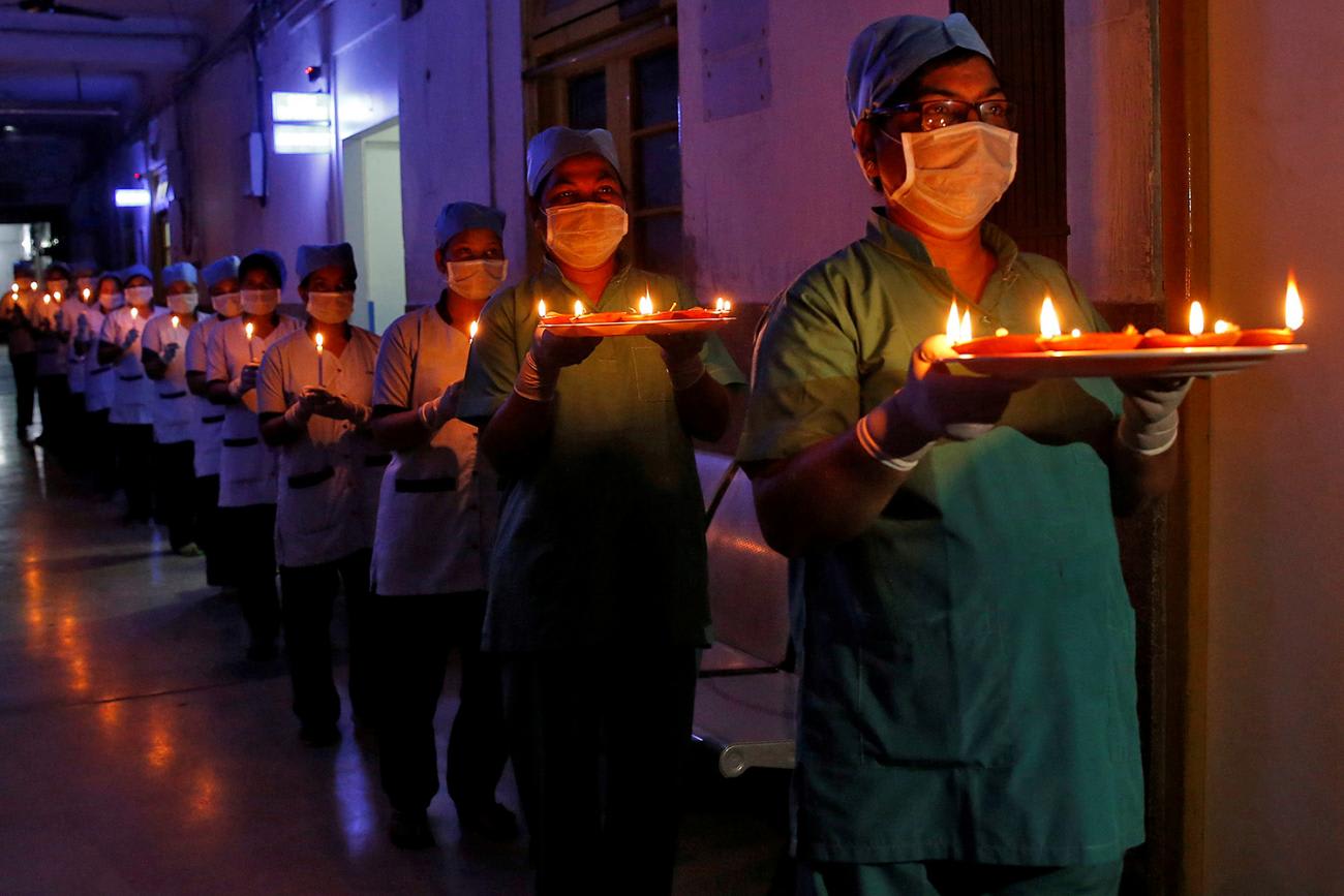 The photo shows a long procession of health care workers carrying candles down a dimply lit corridor.