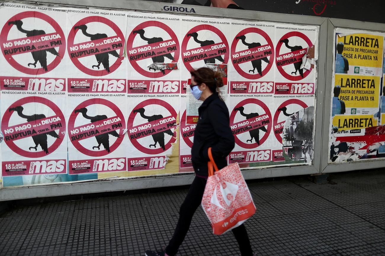 The photo shows a woman walking past a wall on which are plastered dozens of political banners.