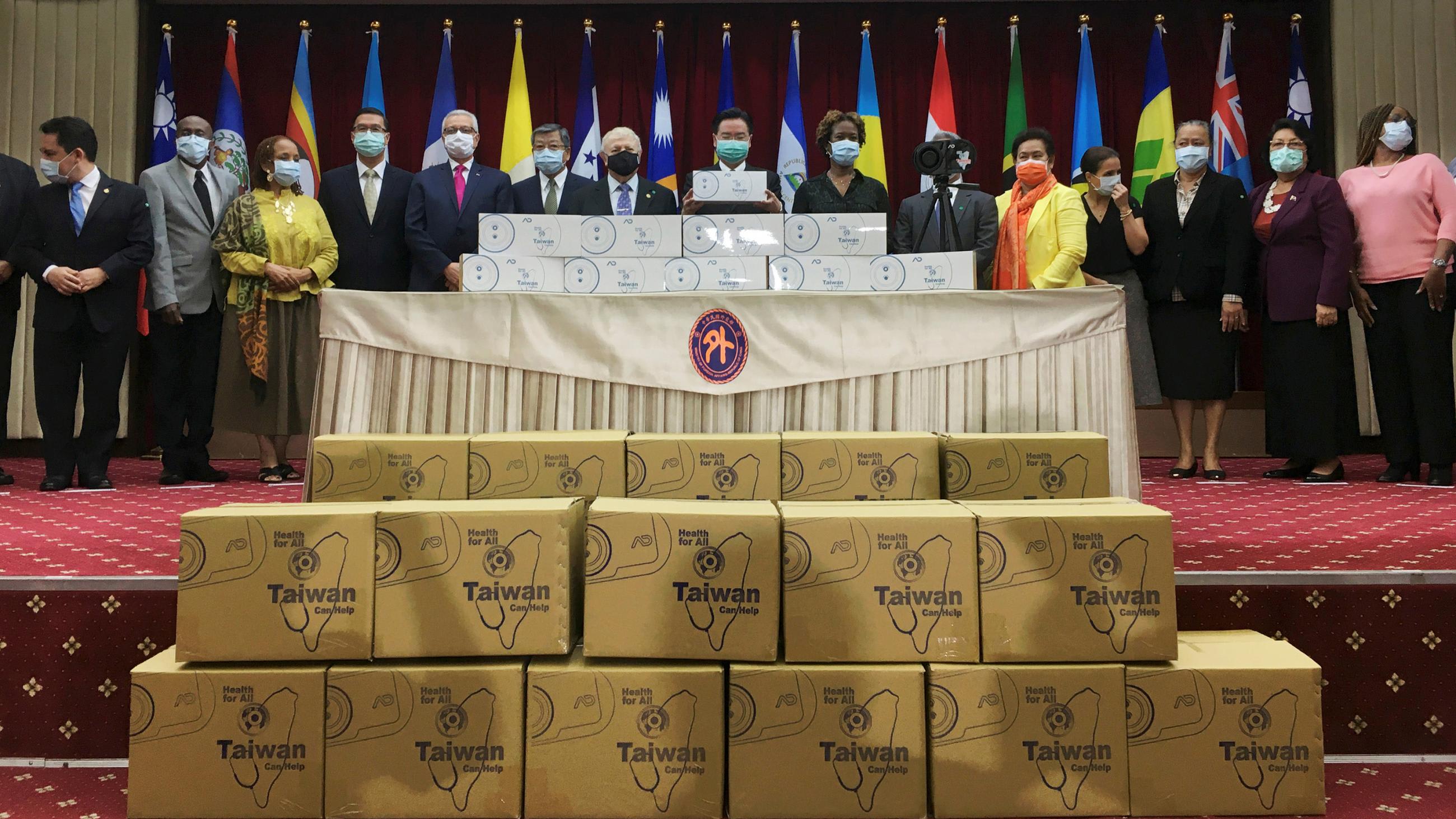 The photo shows a group of dignitaries amidst boxes of goods to be donated.