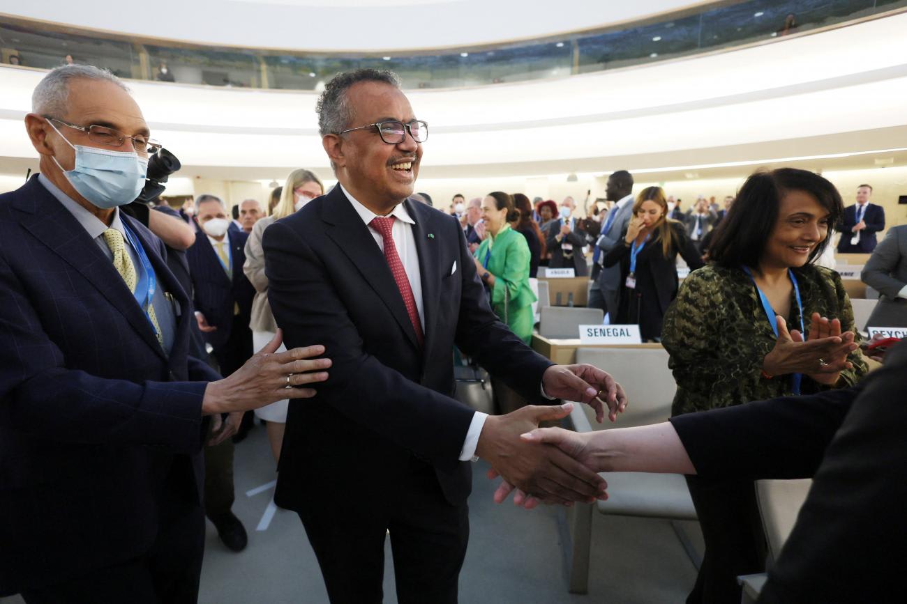 Dr. Tedros Adhanom Ghebreyesus, Director-General of the WHO, wearing a dark suit and red tie, shakes hands with attendees as he elebrates his re-election during the 75th World Health Assembly at the United Nations in Geneva, Switzerland, on May 24, 2022.
