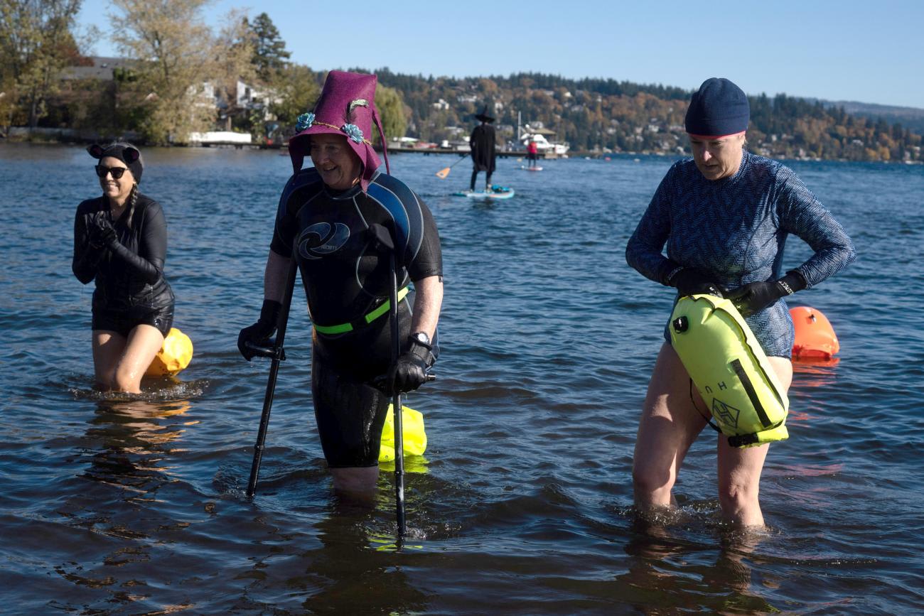Dressed as witches, three swimmers exit the water where people are paddle boarding and kayaking for Halloween on Lake Washington in Seattle, Washington, on October 30, 2021.