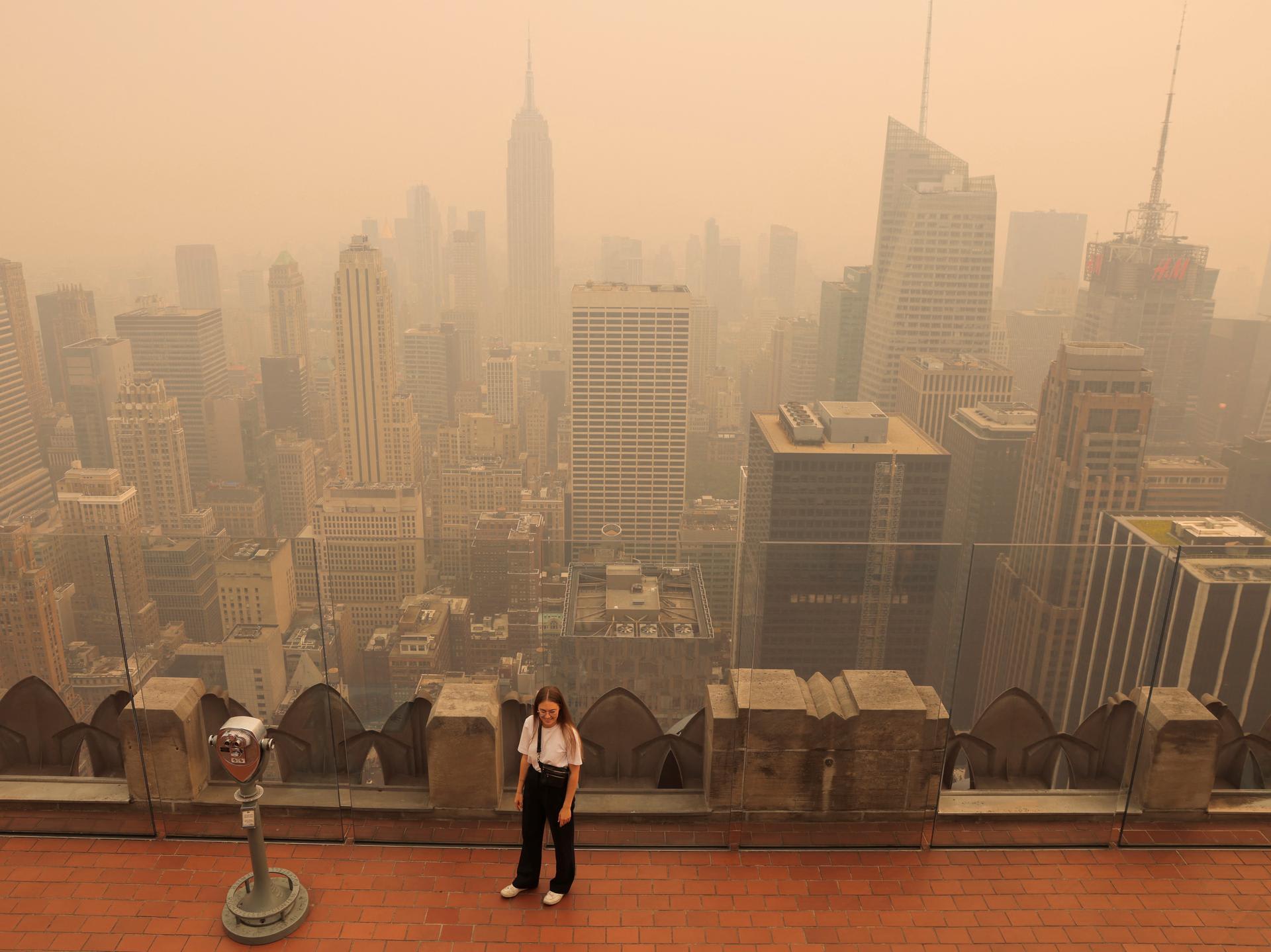 A person visits the top of the Rockefeller Center, as haze and smoke caused by wildfires in Canada hang over the Manhattan skyline.