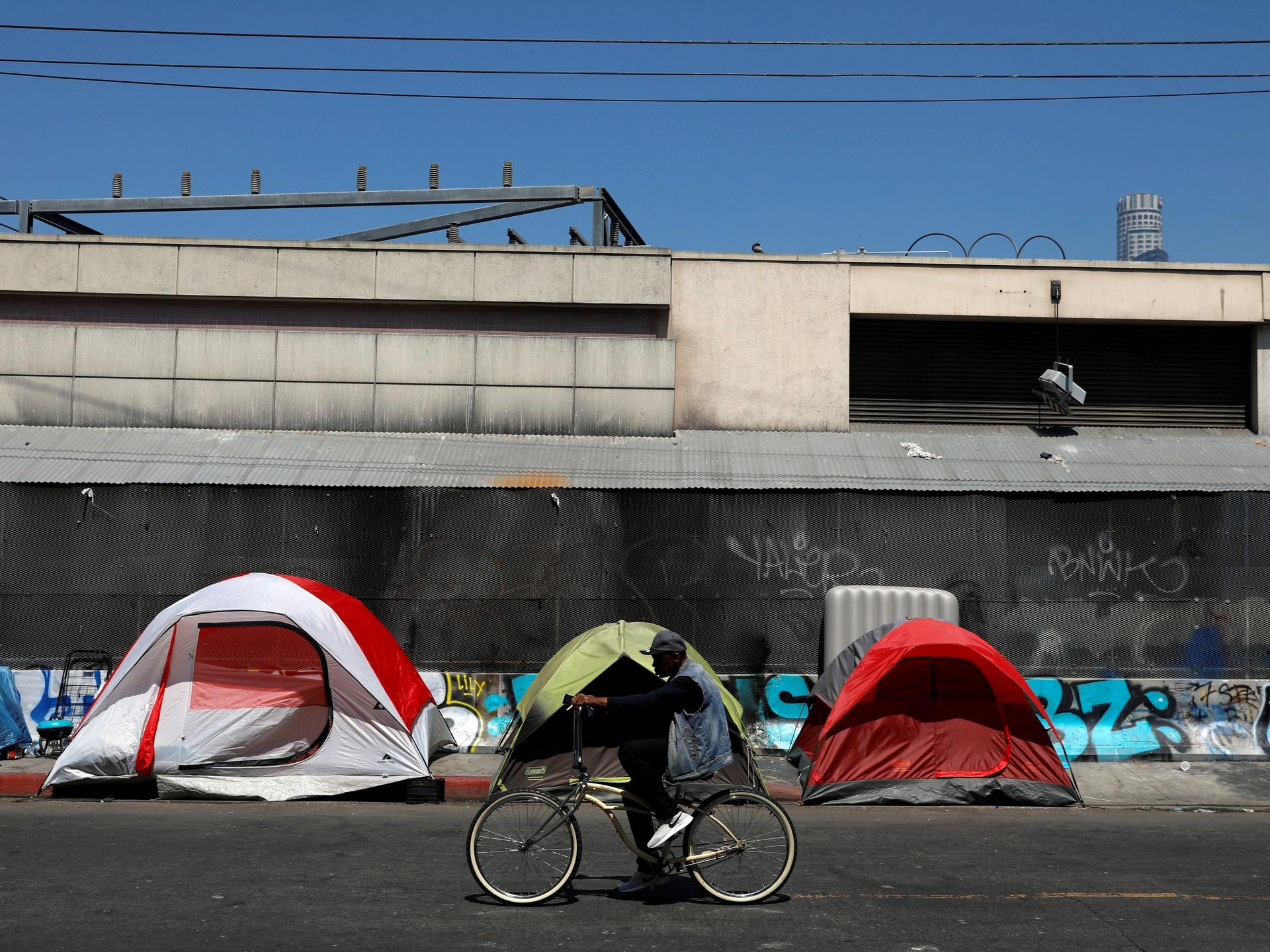 A cyclist passes by tents and tarps erected by homeless people along sidewalks in the skid row area of downtown Los Angeles, California, on June 28, 2019.