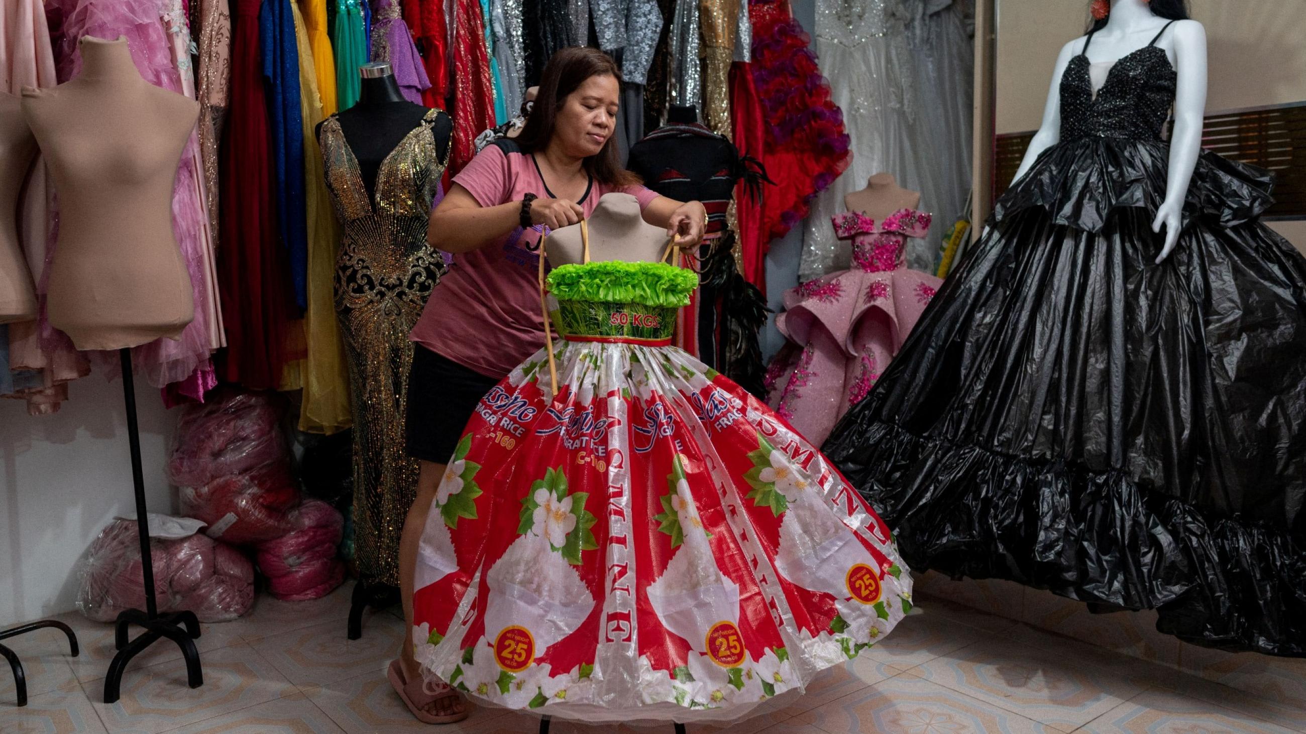 A shopkeeper arranges a pink and green formal dress made out of fabric from recycled bottles