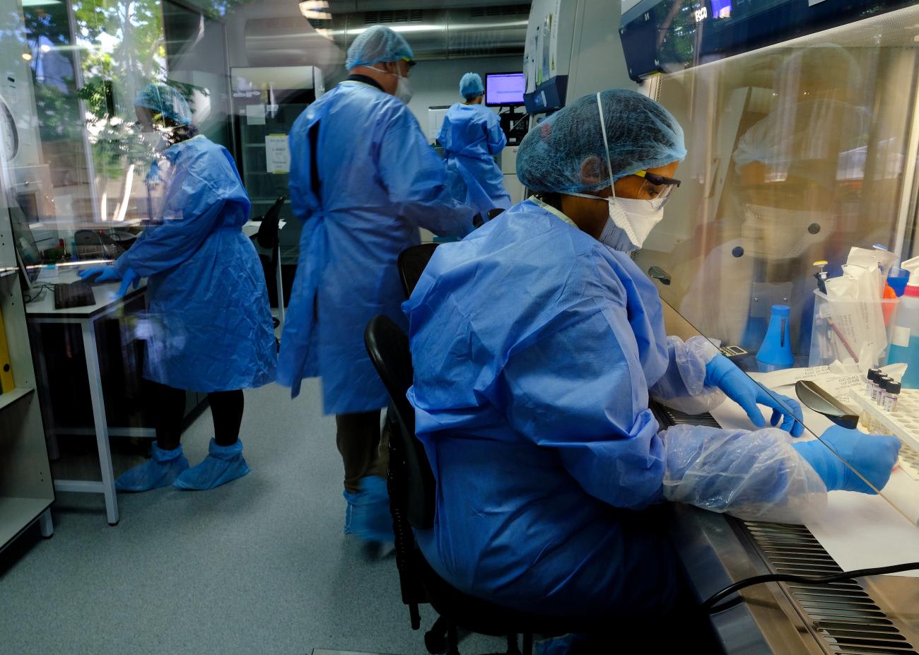 Researchers in blue medical clothing study the BCG vaccine for tuberculosis test samples in a laboratory run by South African biotech company TASK in Cape Town, South Africa, on May 11, 2020.