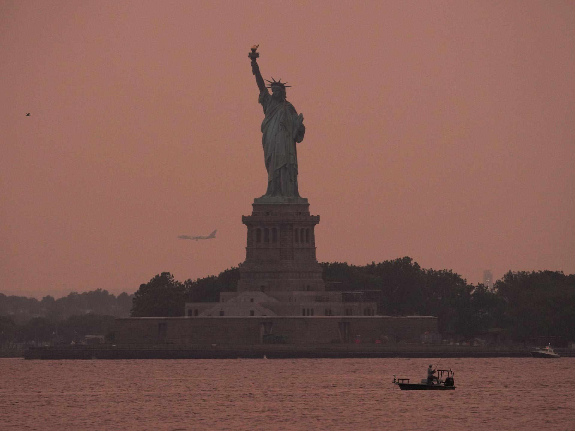 The Statue of Liberty is seen at sunset through haze caused by smoke from Canadian wildfires, as viewed from Brooklyn, New York, August 5, 2025.