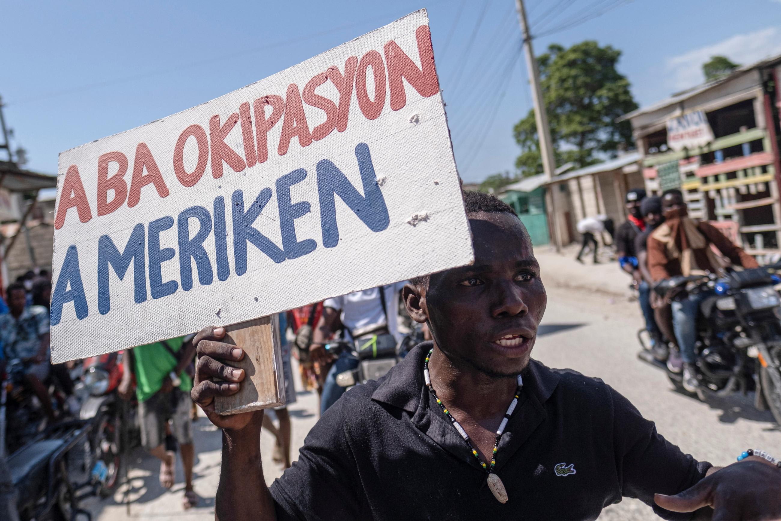 A man holds a placard that reads in Creole 