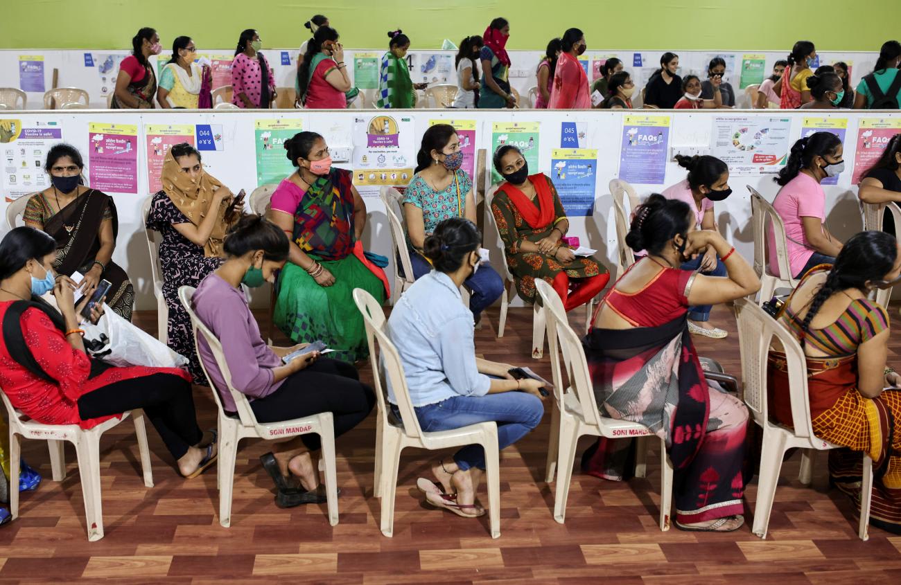 Women sit or stand in three rows, waiting to receive a coronavirus vaccine in India.