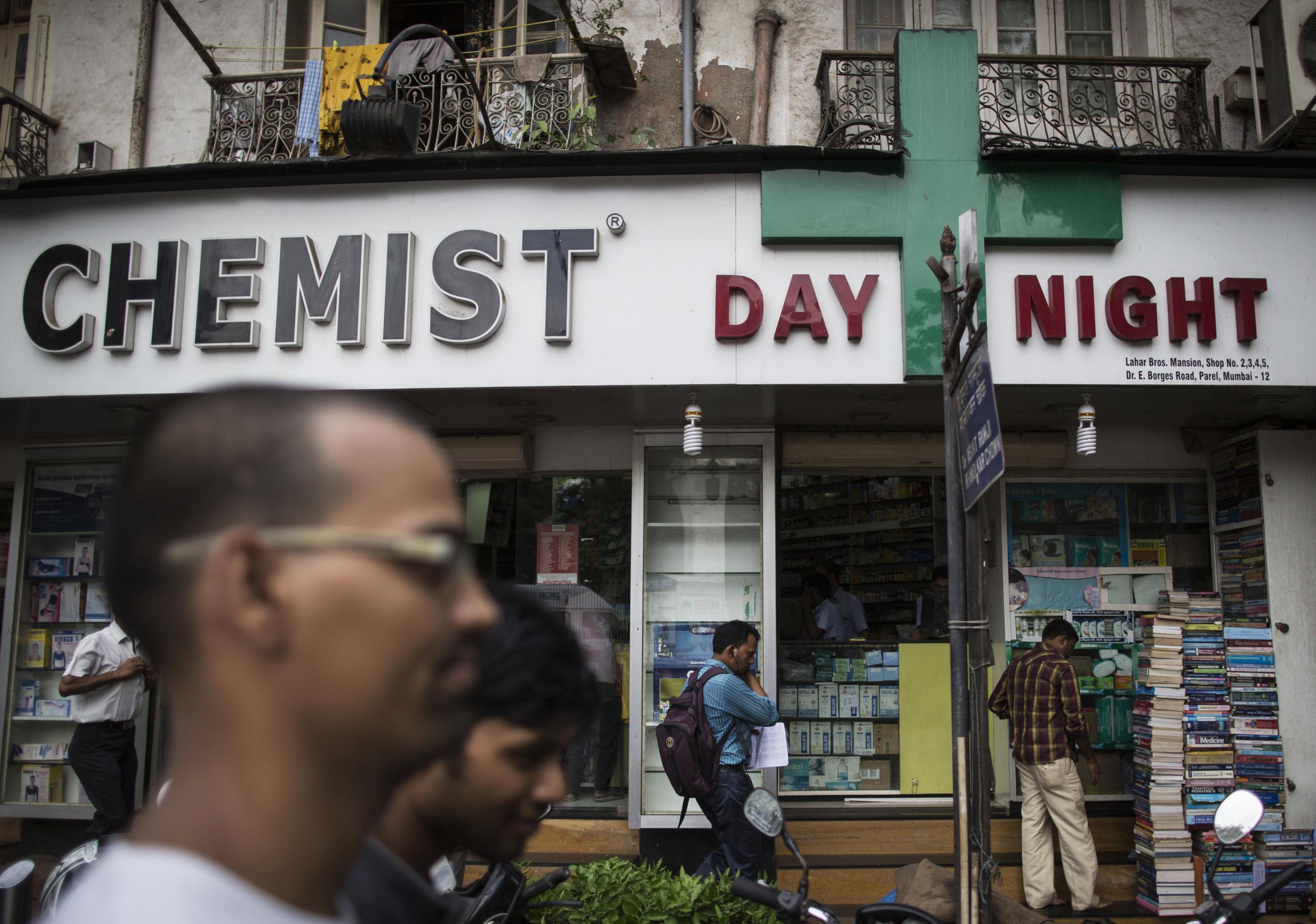 People walk past a chemist shop at a market.