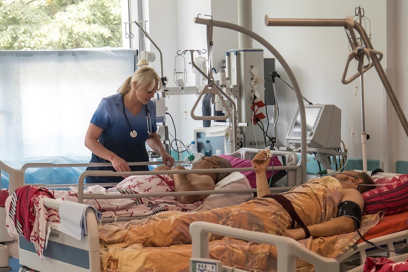 A female medical specialist in blue scrubs attends to a patient who was injured during a Russian missile strike in Vinnytsia, Ukraine. Next to him lies another patient covered in an orange blanket.