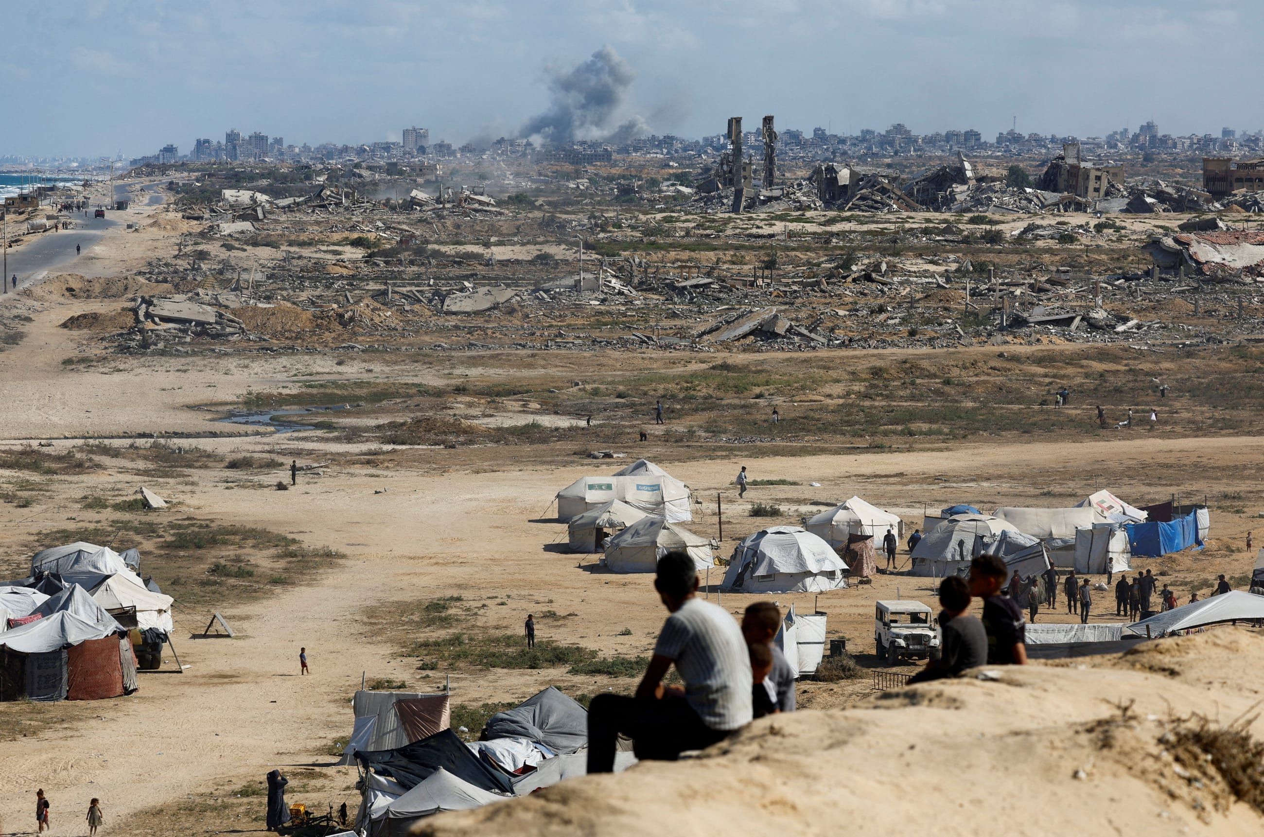 Palestinians look on as smoke rises following explosions, in Gaza City, as seen from central Gaza Strip, on October 5, 2025.
