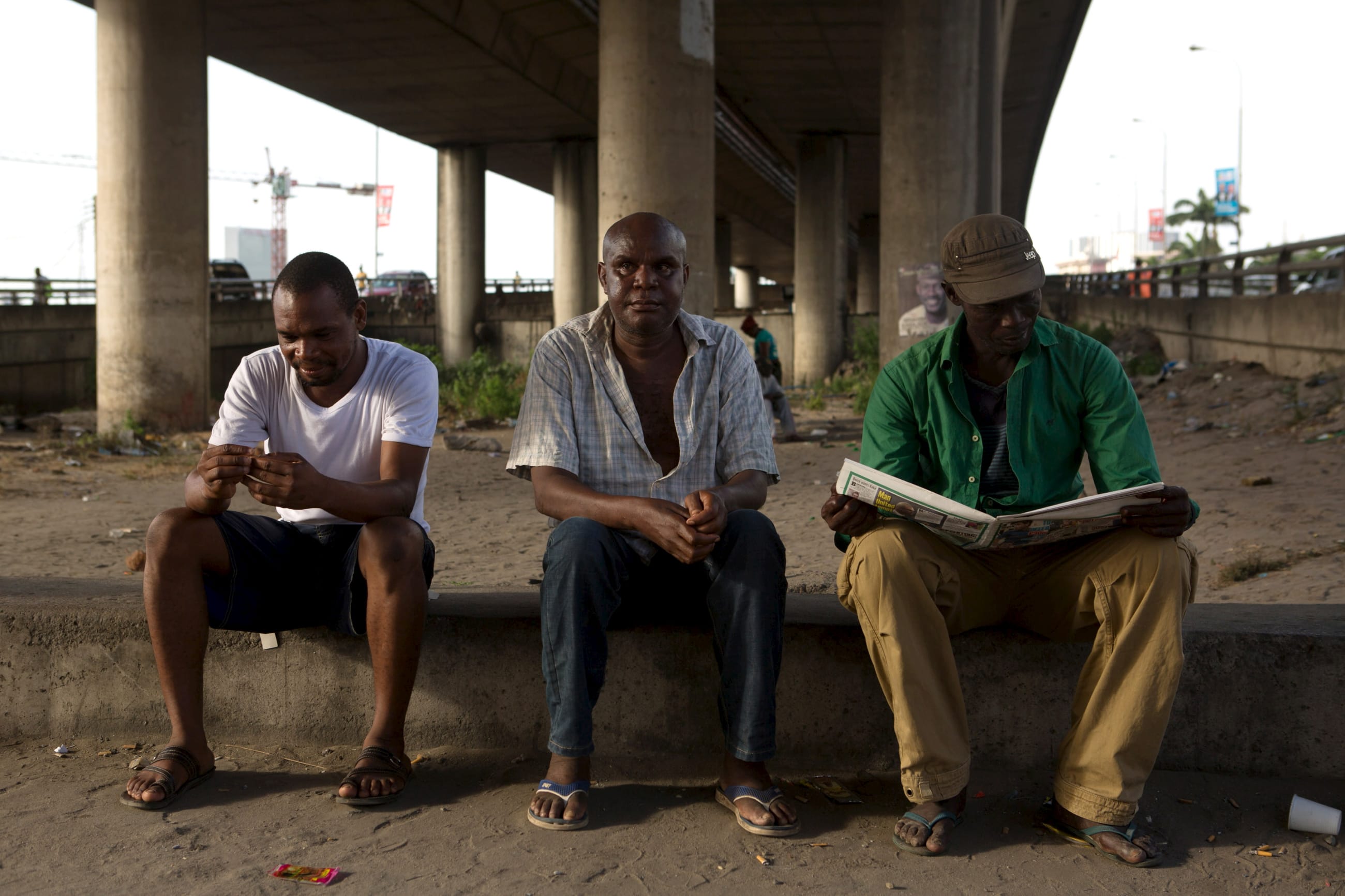 A man reads a newspaper as others sit under a bridge, in Lagos, Nigeria, on March 30, 2015.