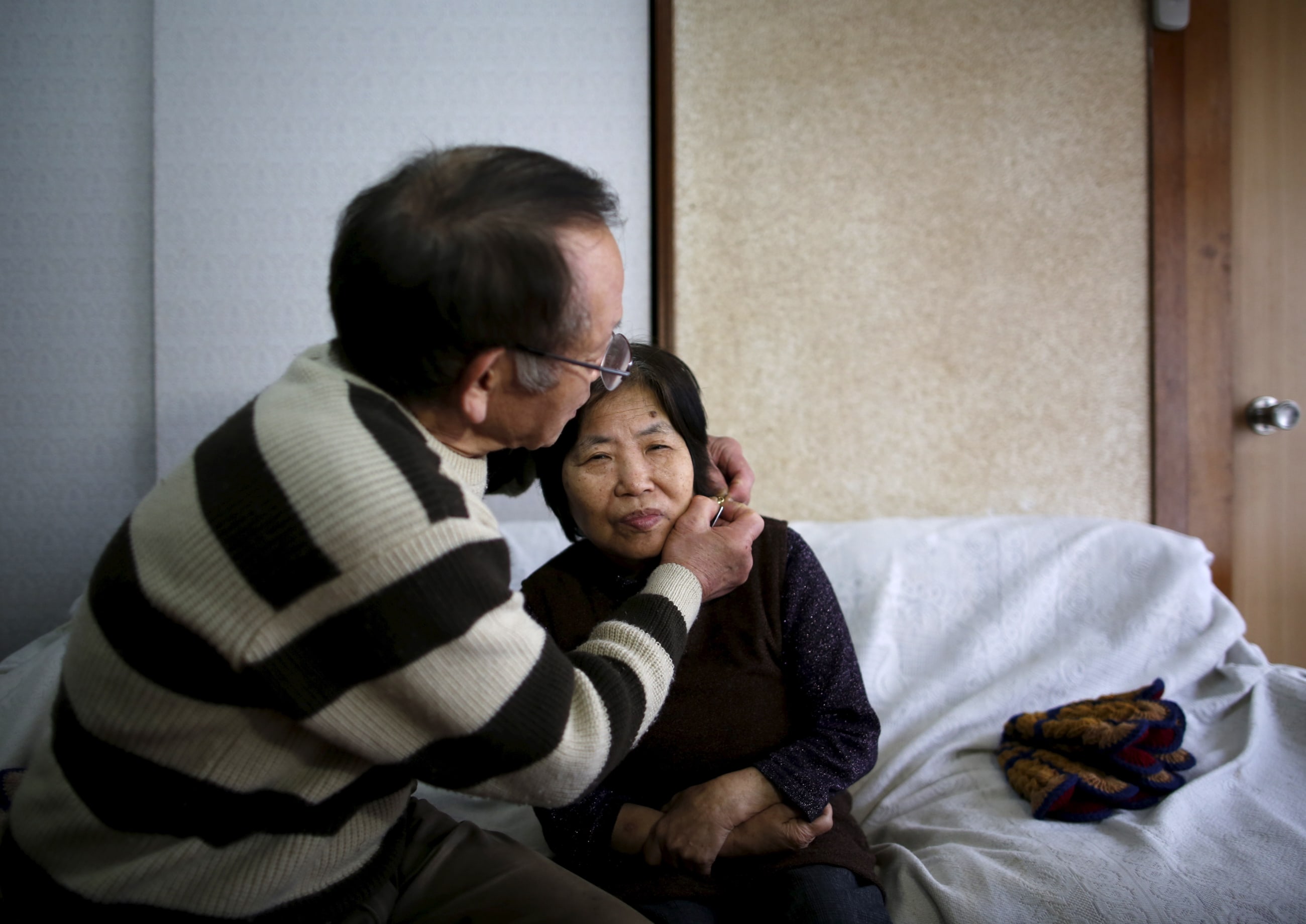 72-year-old Kanemasa Ito (L) puts a GPS tracking necklace on his 68-year-old wife Kimiko who was diagnosed with dementia 11 years ago, on a sofa at their home in Kawasaki, south of Tokyo, Japan, on April 6, 2016.