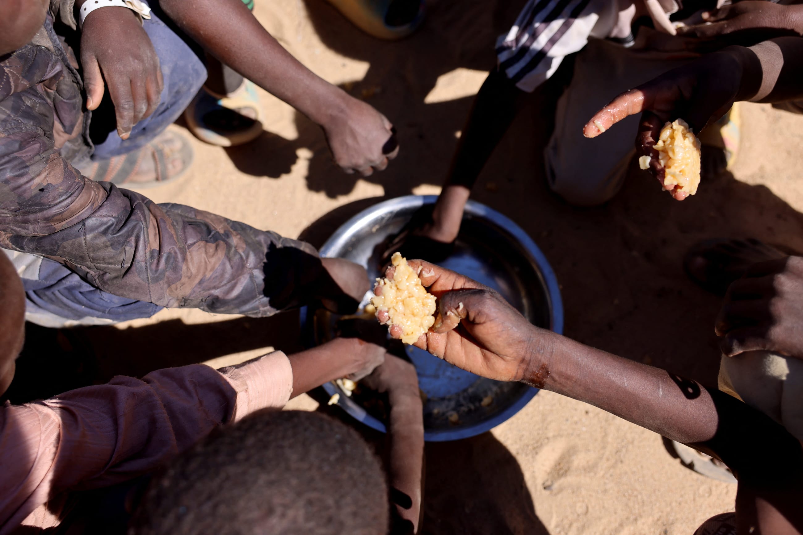 Sudanese orphaned refugees children from al-Fashir share a free meal of pasta and meat provided by the "Group Kitchen Project," led by Najwa Isa Adam, inside the Tine transit camp, in eastern Chad, as they flee ongoing clashes between the paramilitary Rapid Support Forces (RSF) and the Sudanese army, on November 22, 2025.