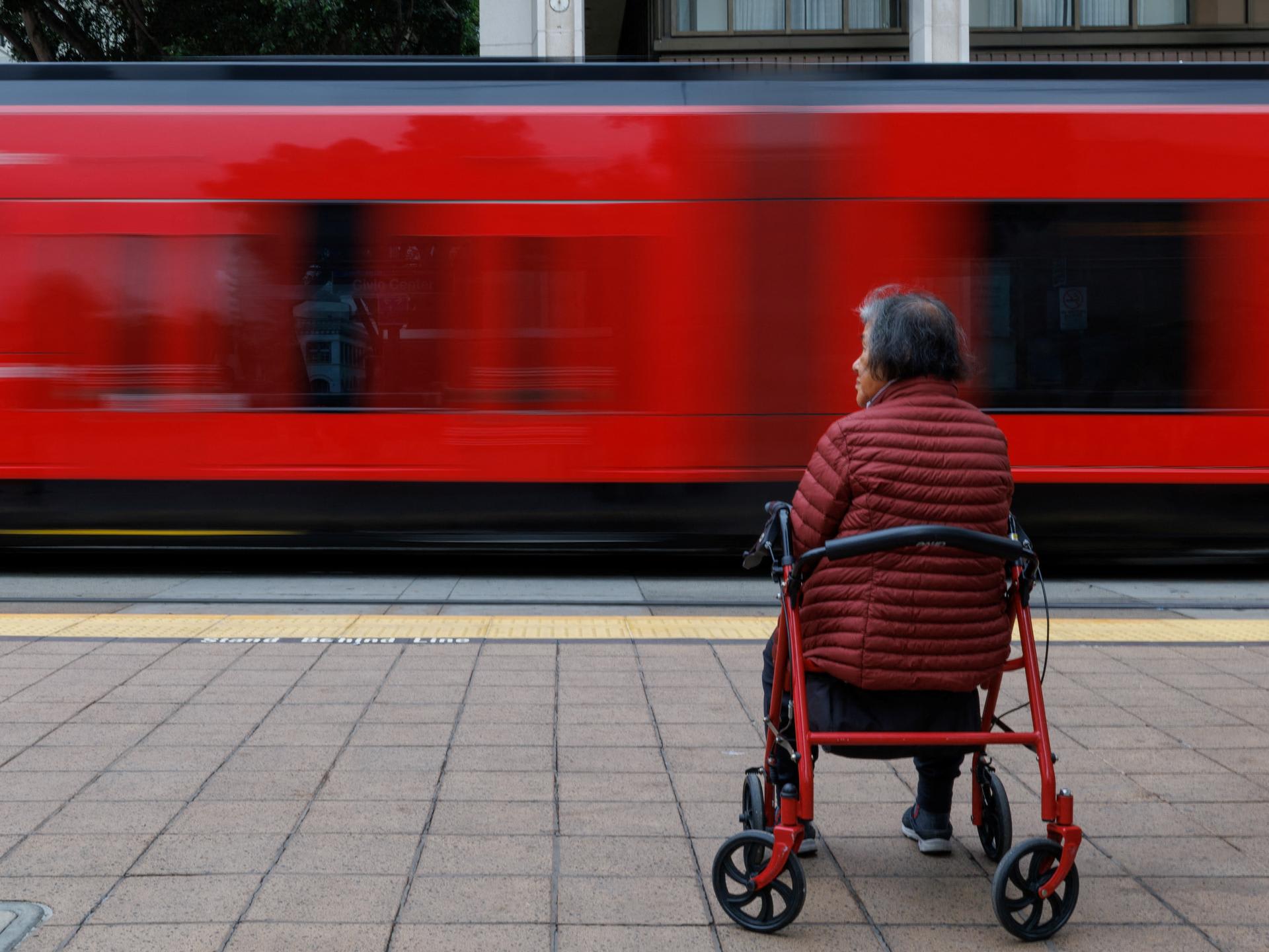 An elderly person sits on their walker while waiting for public transit, in San Diego, California, on March 26, 2025.
