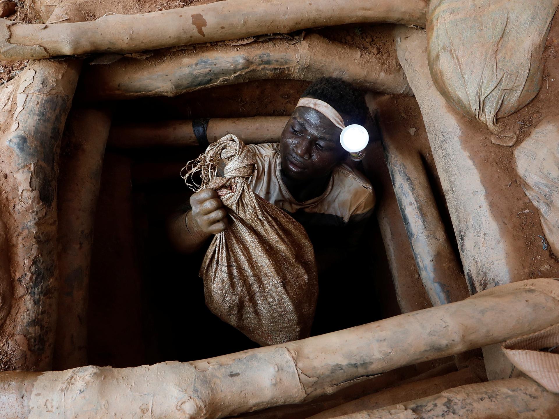 An artisanal miner climbs out of a gold mine with a bag of rocks broken off from inside a mining pit, at the unlicensed mining site of Nsuaem Top, in Ghana, on November 24, 2018.