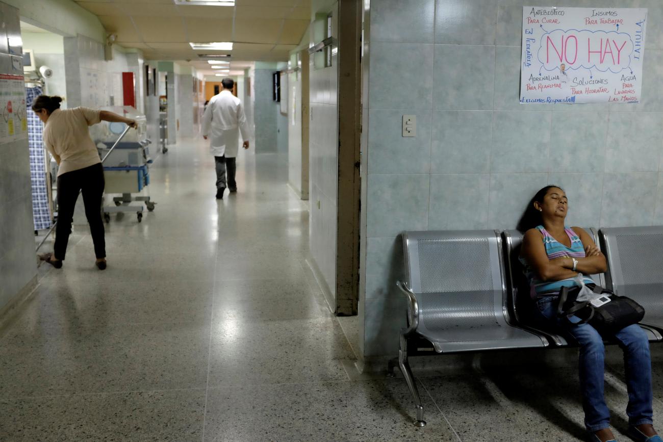 A woman sleeps under a sign that reads "There are not antibiotics to cure," in the pediatric emergency waiting room, at the university hospital, in Merida, Venezuela, on June 17, 2016.