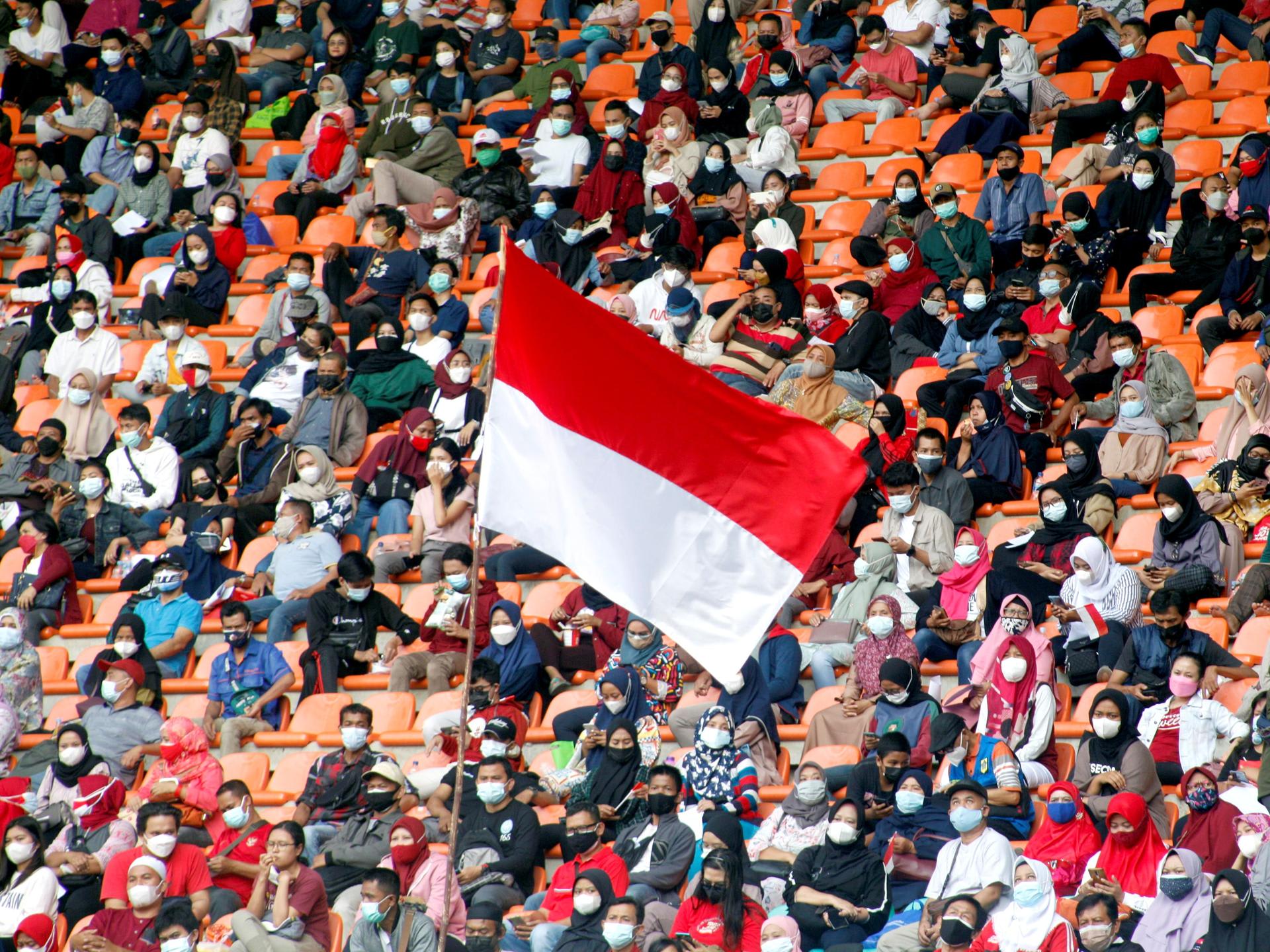 The Indonesian flag flies as people, wearing protective face coverings, wait to receive a COVID-19 vaccine dose, at Pakansari Stadium, in Bogor, Indonesia, on August 14, 2021.