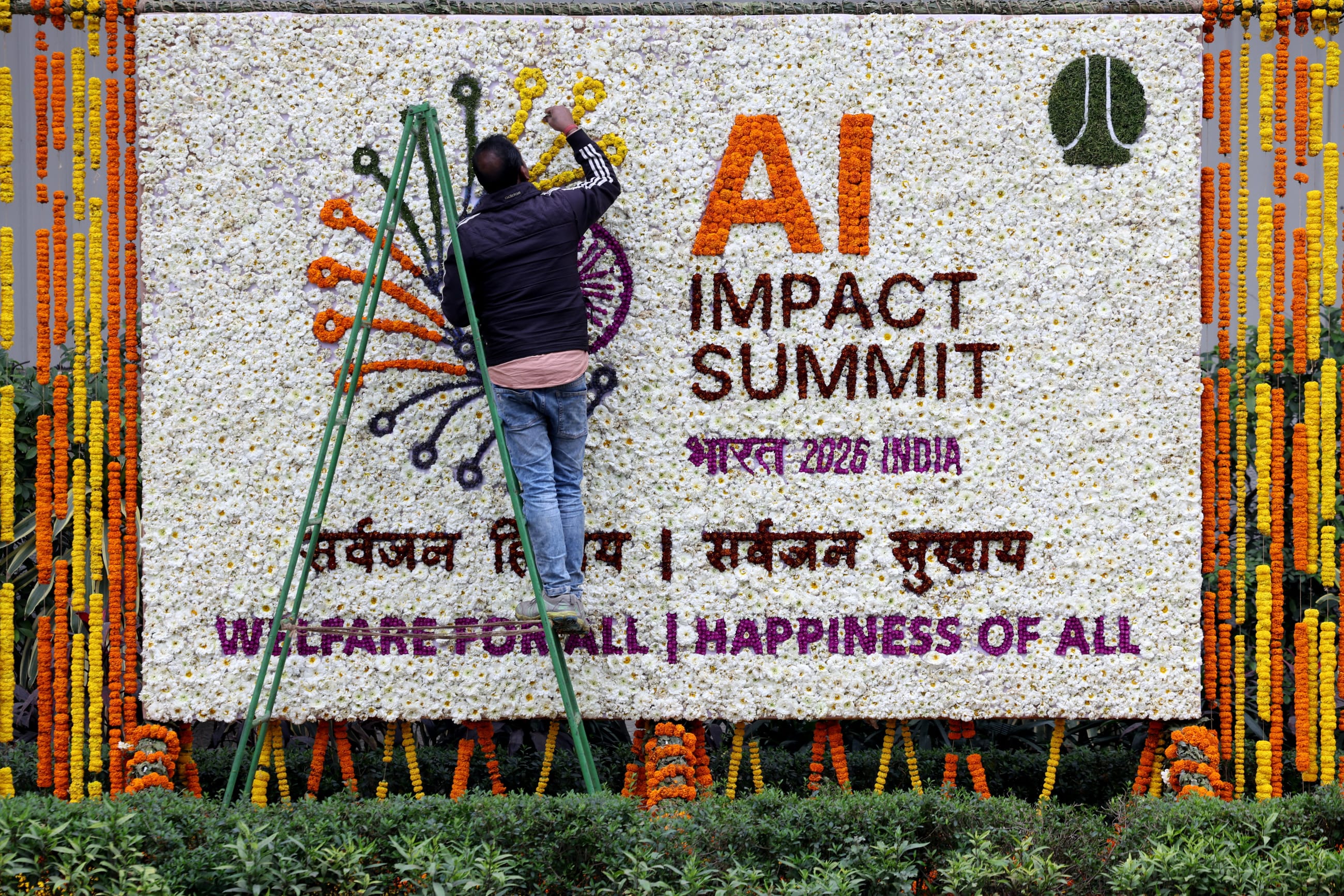 A worker makes a logo of AI Impact Summit out of flowers along a road, in New Delhi, India, on February 18, 2026.