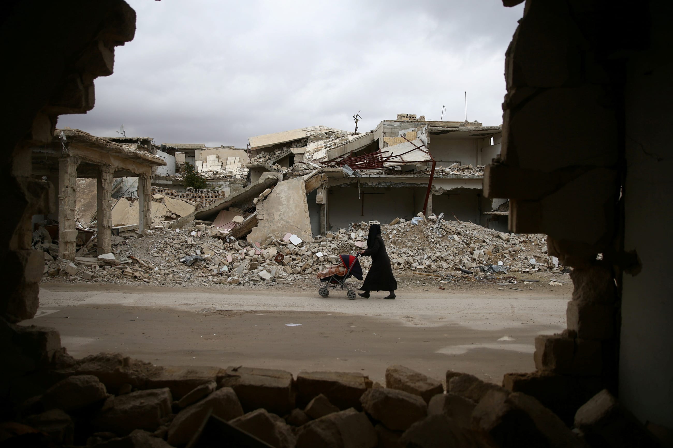 A woman pushes a baby trolley past damaged buildings, in Douma, in the eastern Damascus suburb of Ghouta, Syria, on January 8, 2017.