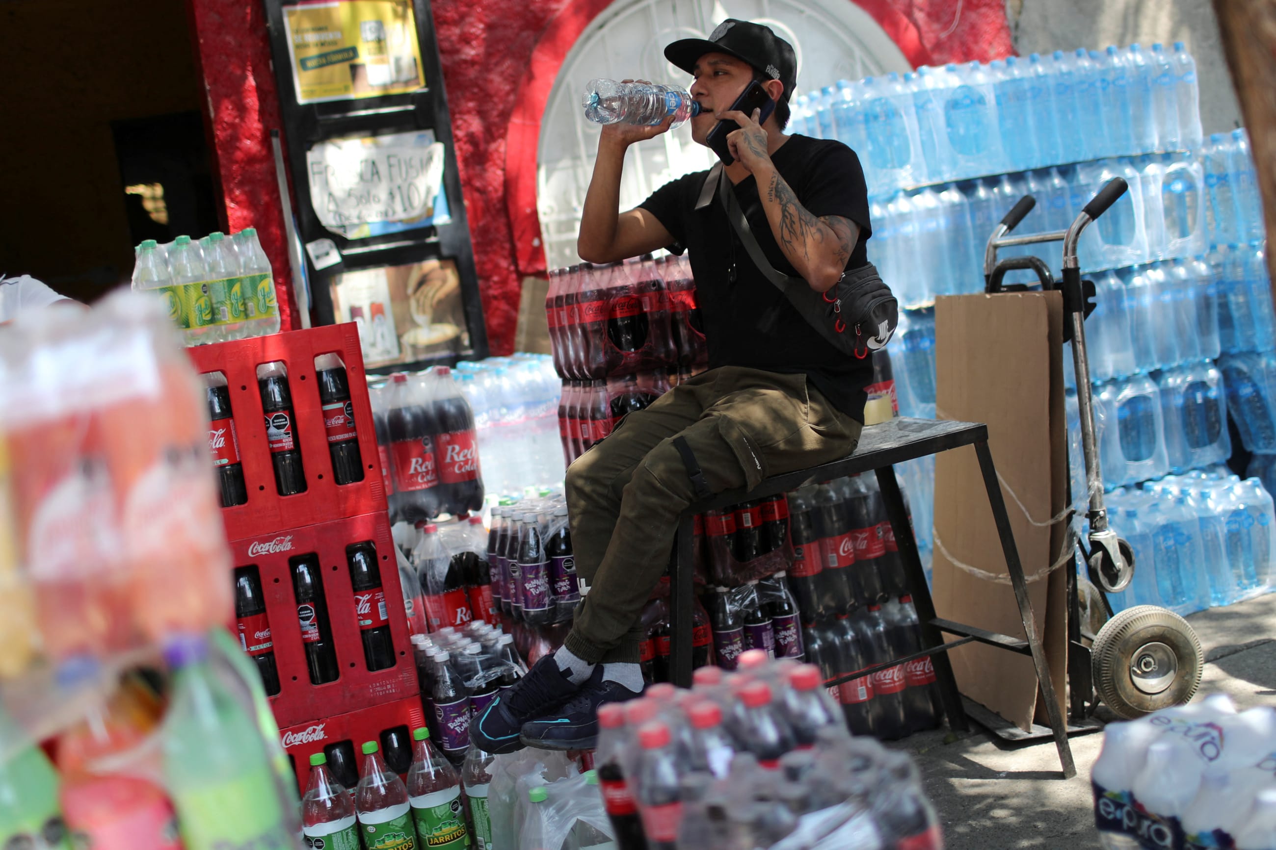 A man drinks water sitting on a soda crate outside a grocery store, in Mexico City, Mexico, on April 16, 2024.