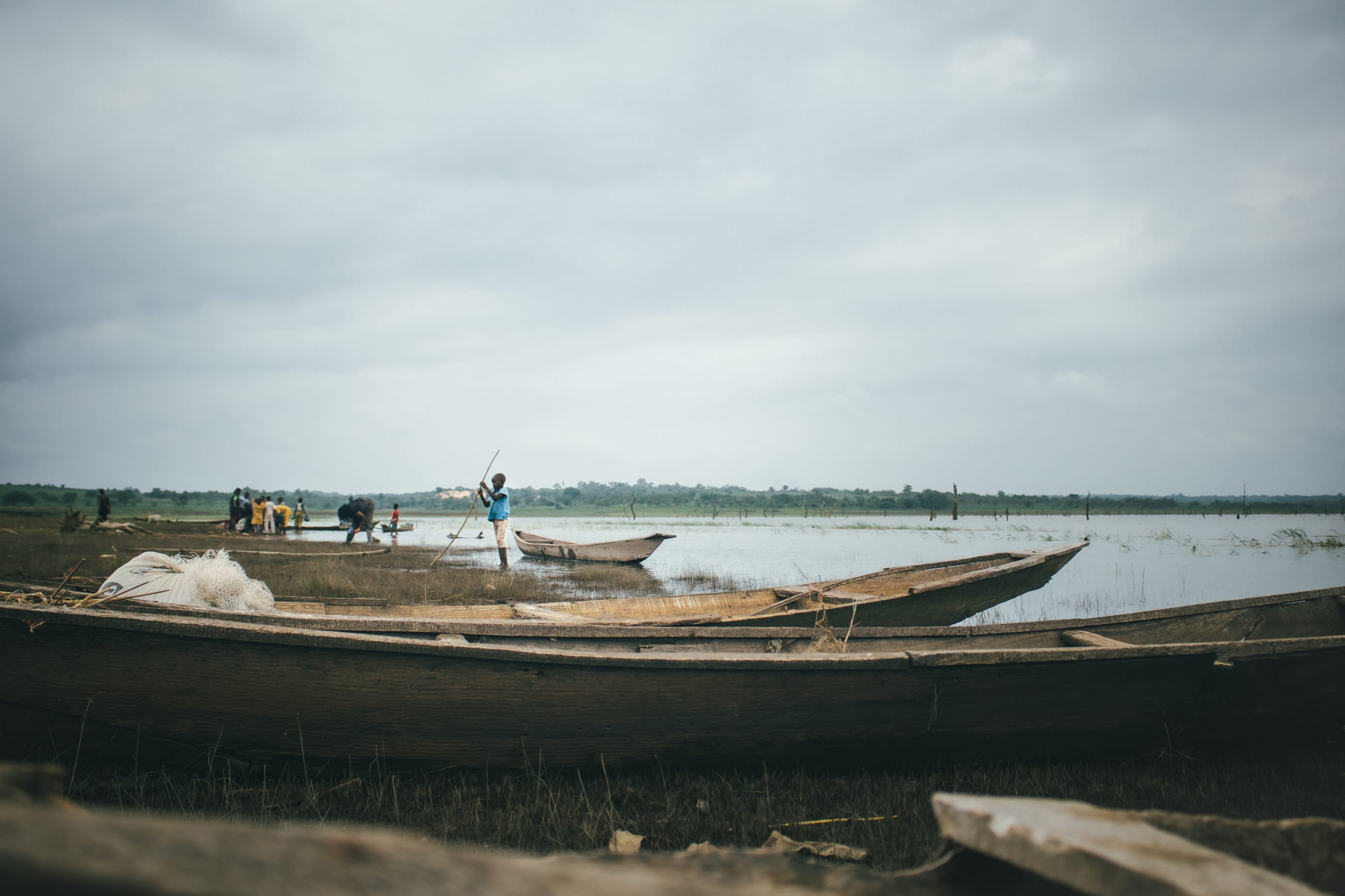 A child checks a fish trap, while researchers work at the waterfront, on July 2025.