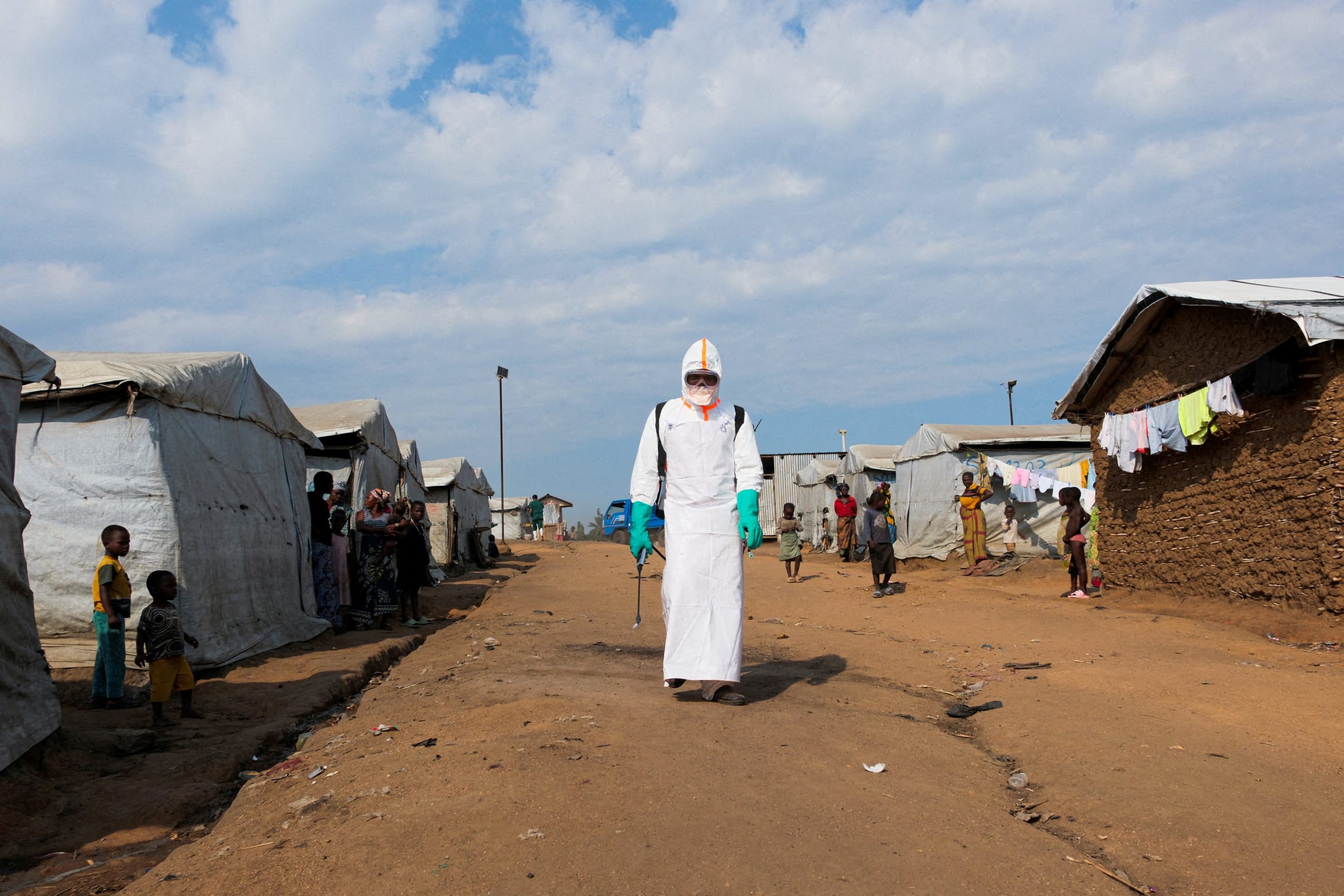 Displaced people watch a health worker in full personal protective equipment (PPE) preparing to disinfect the area during the burial of suspected Ebola victims, in Bunia, eastern Democratic Republic of Congo, on June 18, 2026.