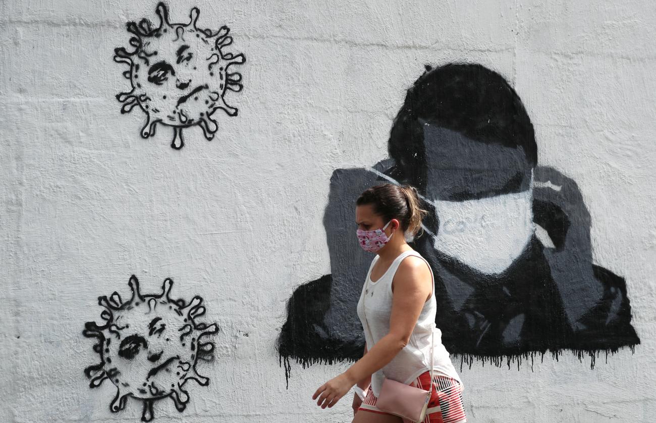 A woman walks past by a graffiti depicting Brazil's President Jair Bolsonaro adjusting his protective face mask and viruses, amid the coronavirus disease (COVID-19) outbreak in Rio de Janeiro, Brazil on July 2, 2020.